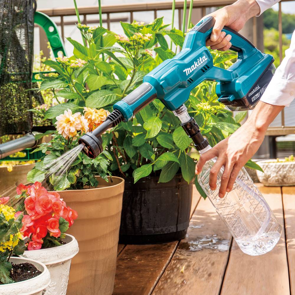 Person, die einen schnurlosen Makita-Sprüher verwendet, um Topfblumen und Pflanzen auf einer sonnigen Terrasse zu bewässern.