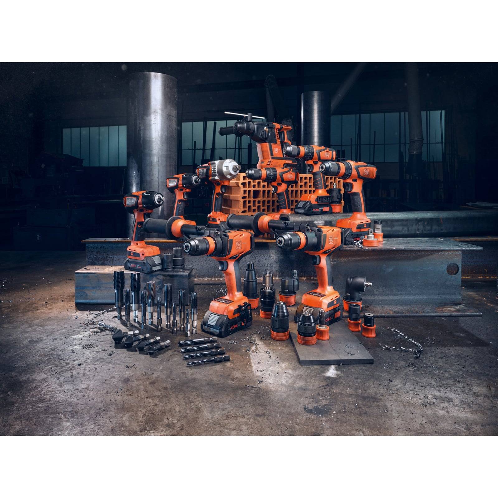 Eine Gruppe orangefarbener Elektrowerkzeuge, einschließlich Bohrmaschinen und Sägen, in einer Werkstattumgebung angeordnet, mit Metallträgern und Werkzeugen auf dem Boden.