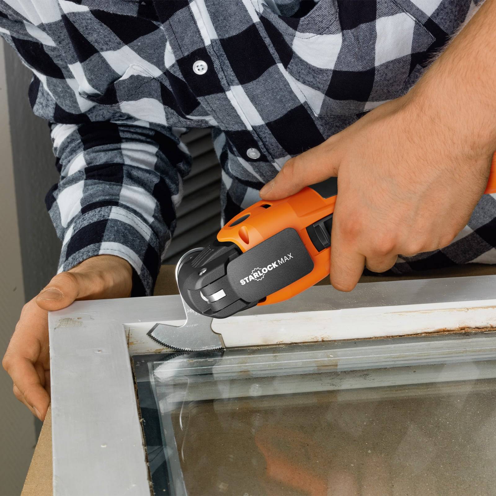 Eine Person, die ein orangefarbenes und schwarzes oszillierendes Multitool verwendet, um einen Metallfensterrahmen zu schneiden und dabei Fenterentfernung oder -reparatur demonstriert.