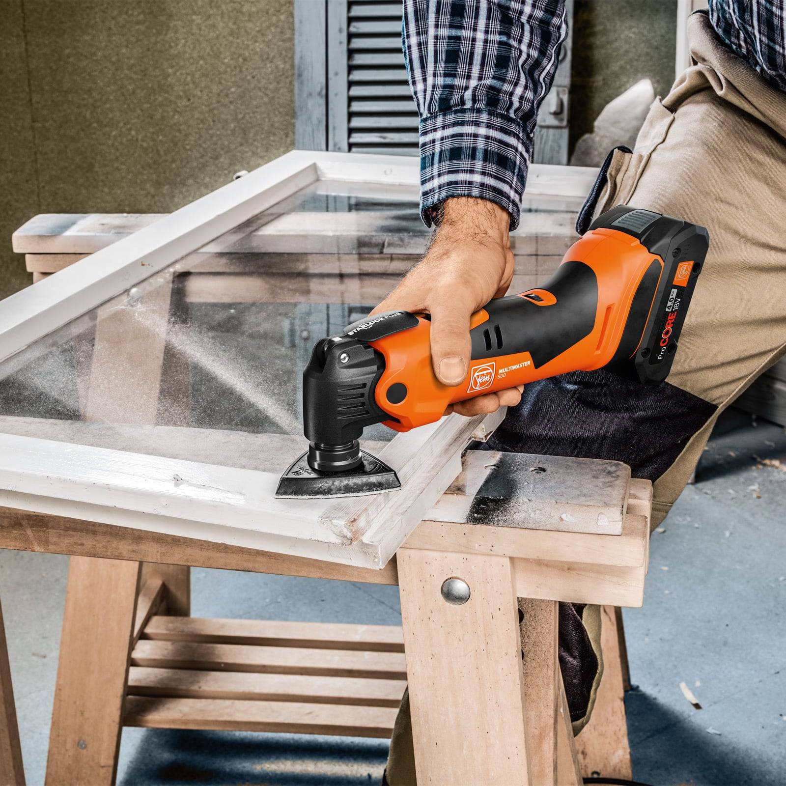 Eine Person benutzt ein Elektrowerkzeug, um die Kante einer Glas- oder Plexiglasscheibe in einer Werkstattumgebung auf einem Holzbock zu trimmen.
