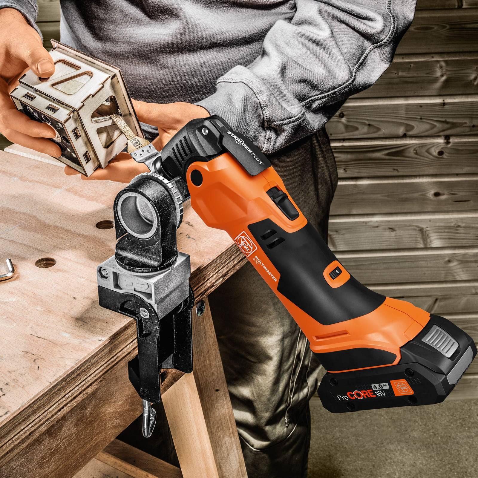 Eine Person verwendet ein kabelloses Orange-Schwarz-Elektrowerkzeug mit einem eingeklemmten Metallstück auf einer Holzwerkbank.
