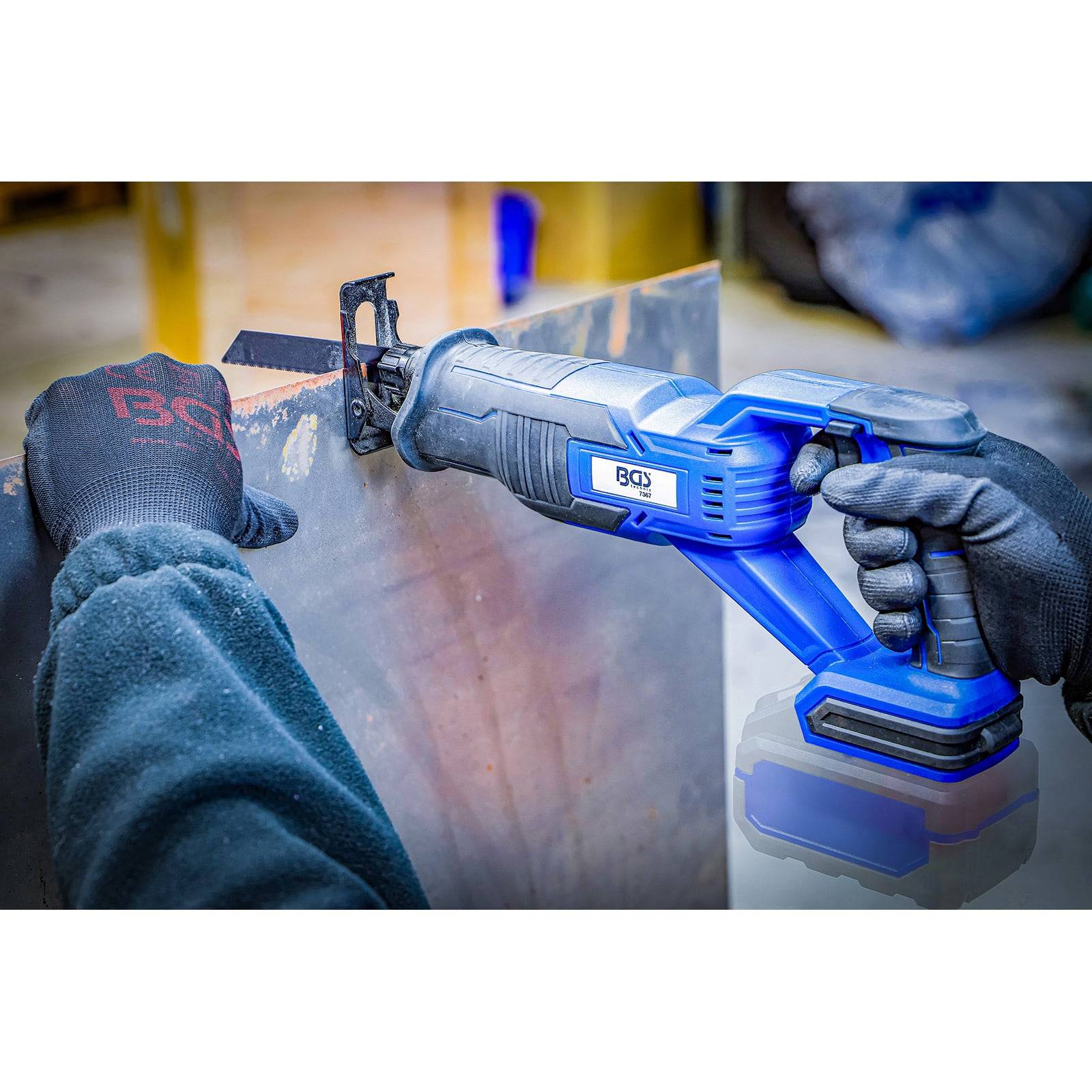 Eine Person benutzt eine blaue tragbare Reciprocating-Säge und schneidet durch ein Metallblech. Sie trägt Schutzhandschuhe und eine dunkle Jacke.