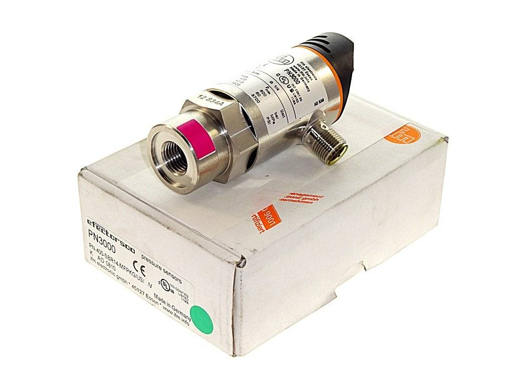 Ein industrieller Drucksensor aus Metall liegt auf einer weißen Produktverpackung, abgebildet in einer Produktfotografie vor einem schlichten Hintergrund.