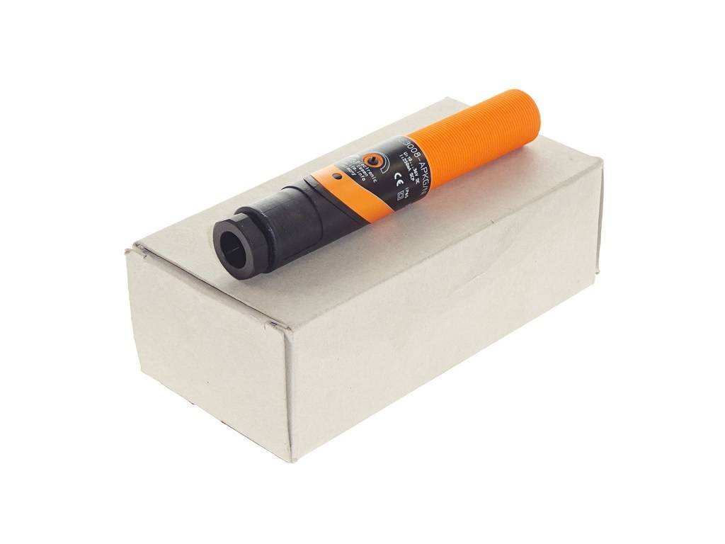 Ein orangefarbenes und schwarzes Handgerät liegt auf einer schlichten weißen Schachtel vor weißem Hintergrund.