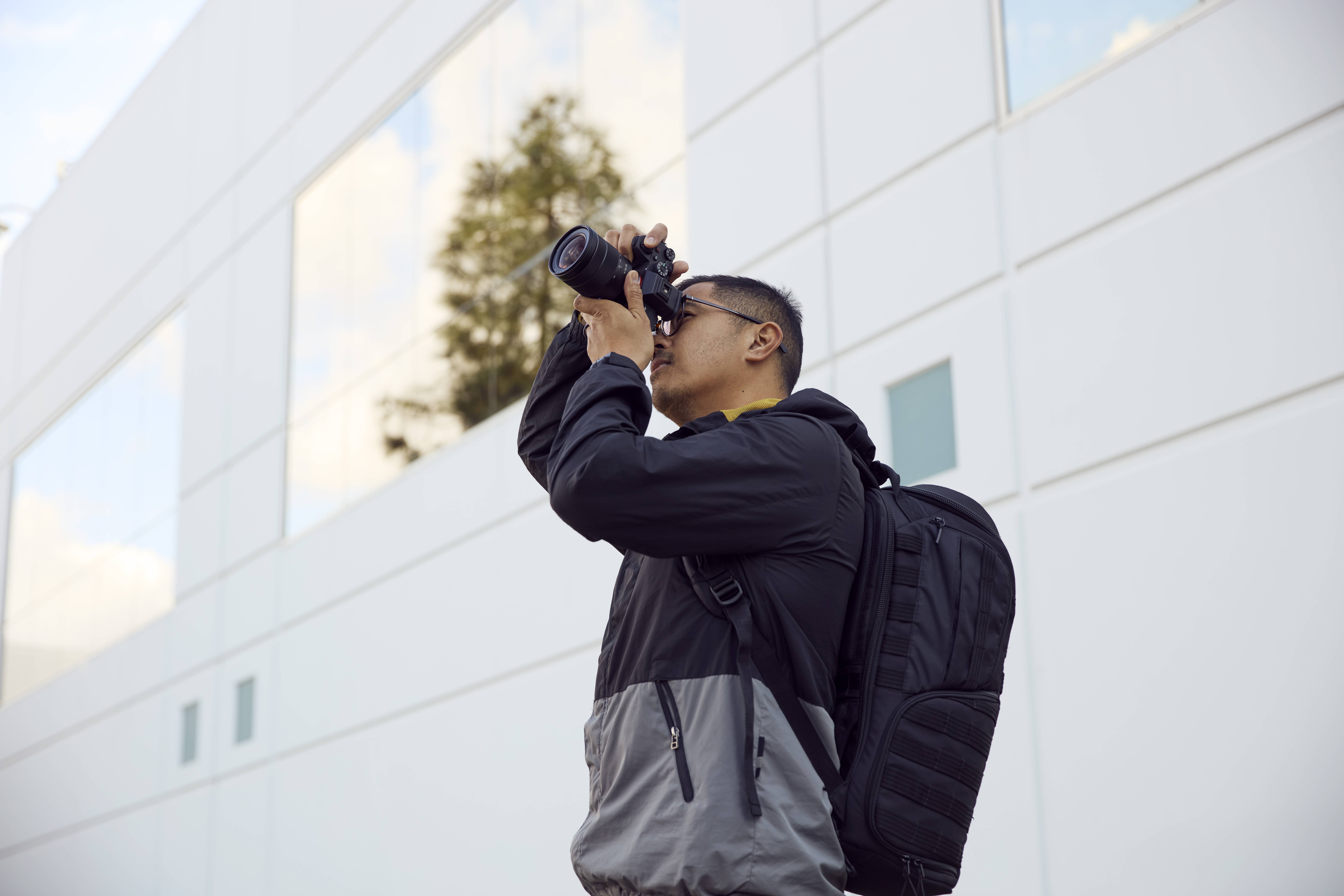 Ein Mann mit Rucksack fotografiert eine moderne Gebäudefassade mit einer Kamera.