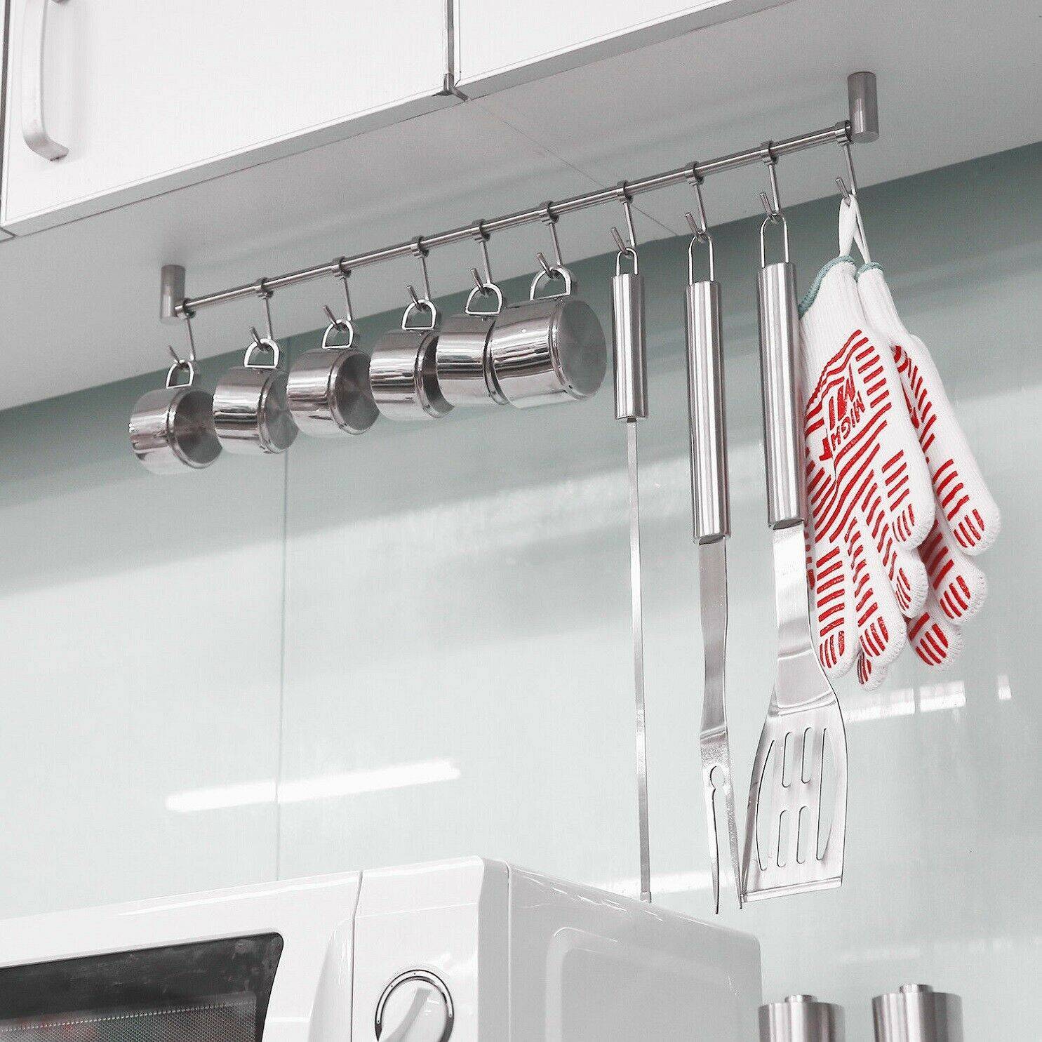 Eine elegante Kücheneinrichtung mit Küchenutensilien und Tassen aus Edelstahl, die an einer Stange hängen, über einer Mikrowelle, mit Topfhandschuhen daneben.