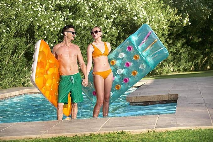 Ein Paar in Badeanzügen steht in einem Pool und hält aufblasbare Schwimmringe, einen orangefarbenen und einen blauen, neben einem Garten-Swimmingpool.