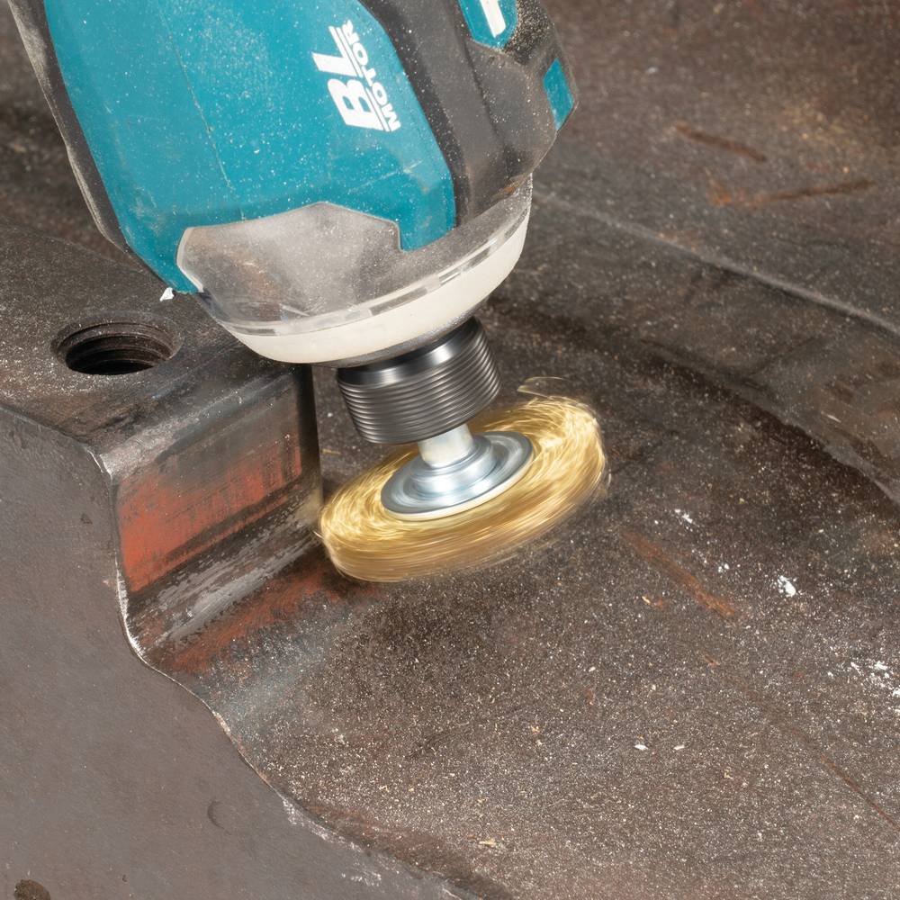 Ein tragbares Elektrowerkzeug mit einer rotierenden Drahtbürste reinigt Rost von einer Metalloberfläche und erzeugt dabei einen hellen kreisförmigen Unschärfeeffekt.