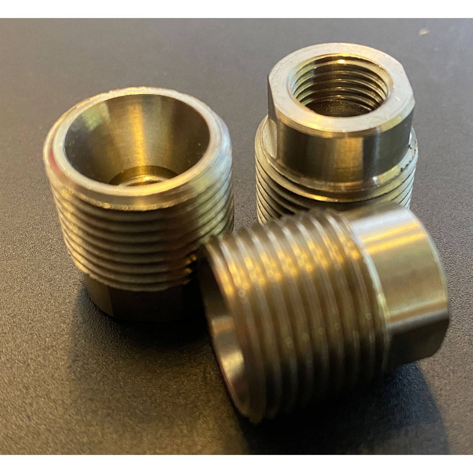 Drei metallene Gewindeanschlüsse auf einer dunklen Oberfläche, die verschiedene Winkel und reflektierende Oberflächen zeigen und auf industrielle Verwendung hindeuten.