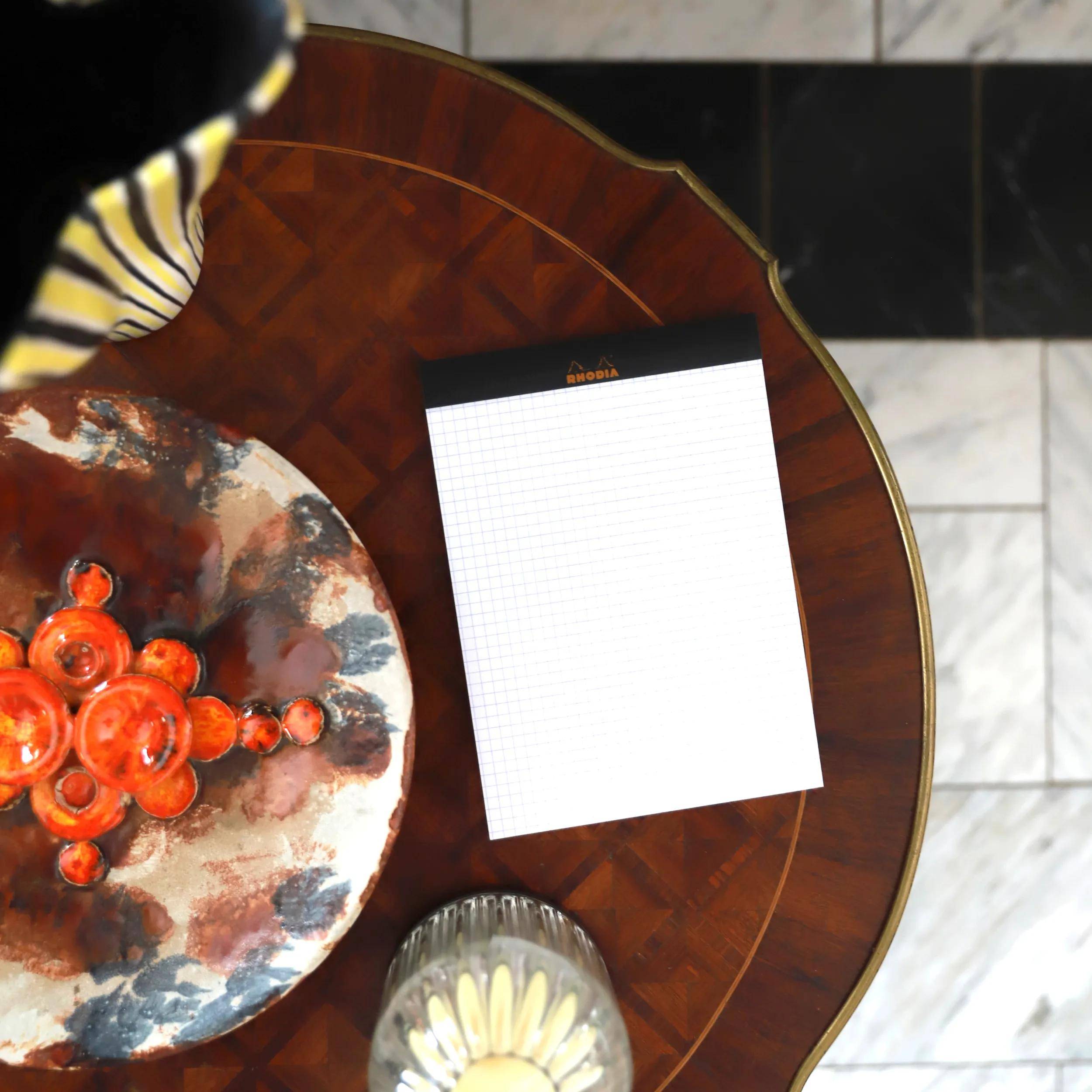 Ein Holztisch trägt eine bunte Keramikschüssel und ein leeres Notizbuch, was auf einen Platz zum Notizenmachen oder Planen hindeutet.