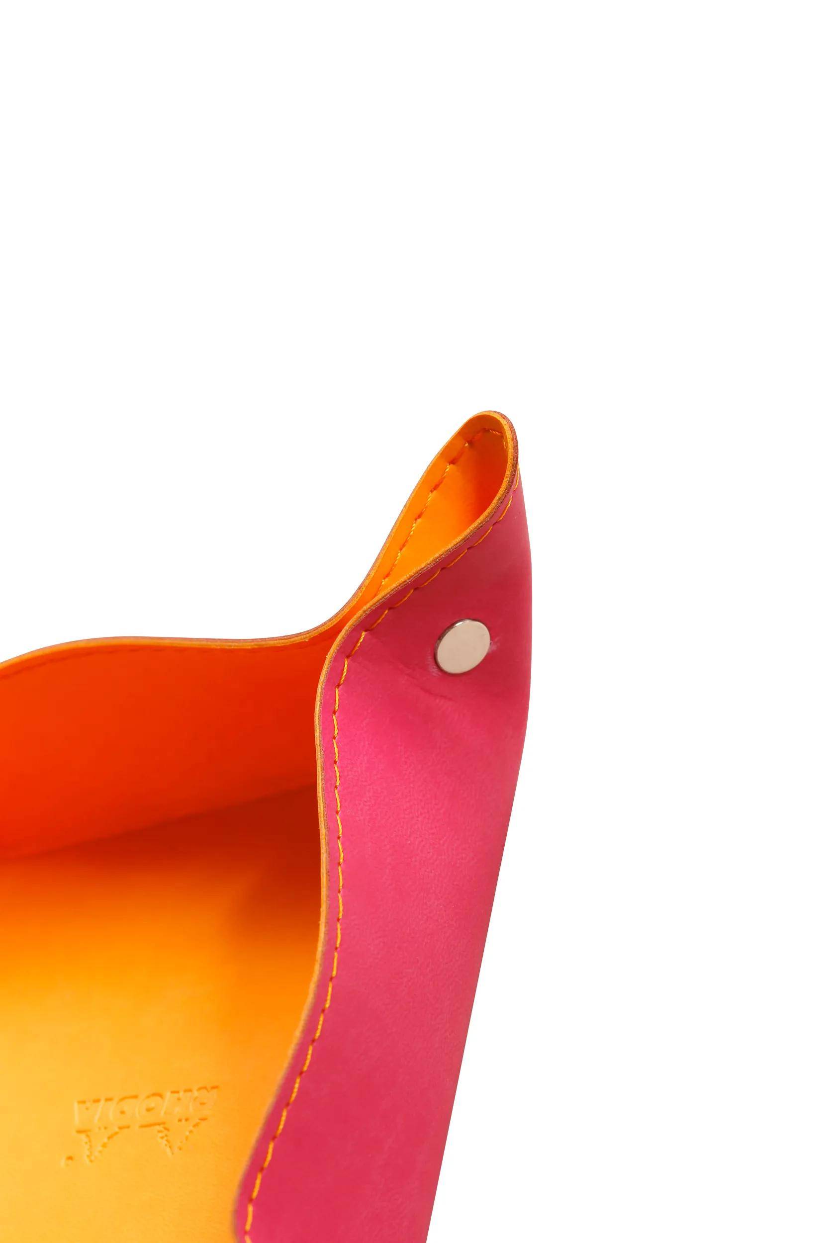 Nahaufnahme einer bunten Tote oder eines Korbs mit rosa und orangen Paneelen, gesäumten Kanten und einem Metallniet auf weißem Hintergrund.