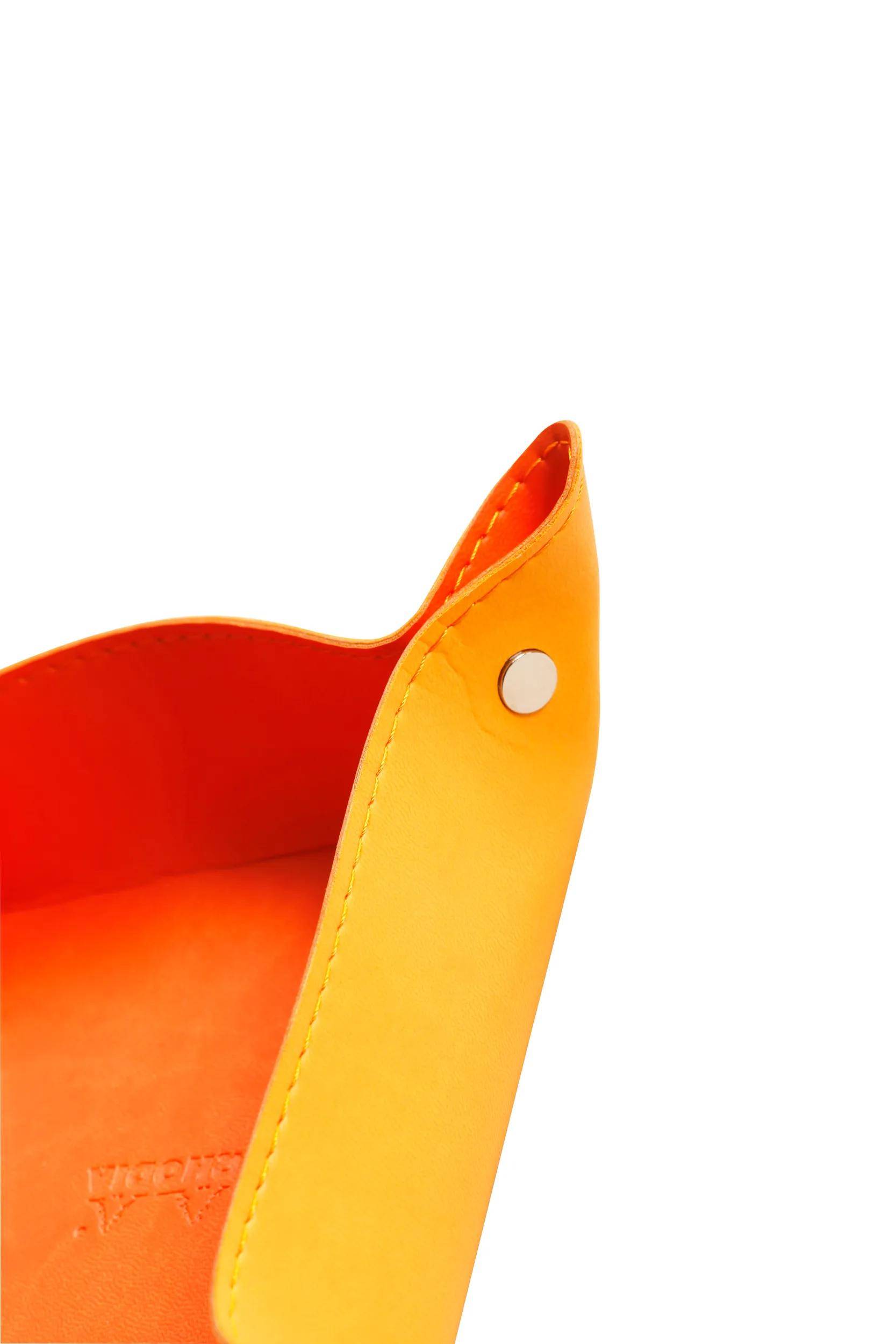 Eine Nahaufnahme einer leuchtend orangefarbenen Ärmel- oder Taschenkante mit einem Metalldruckknopf, die glatte Nähte und starken Farbkontrast zeigt.