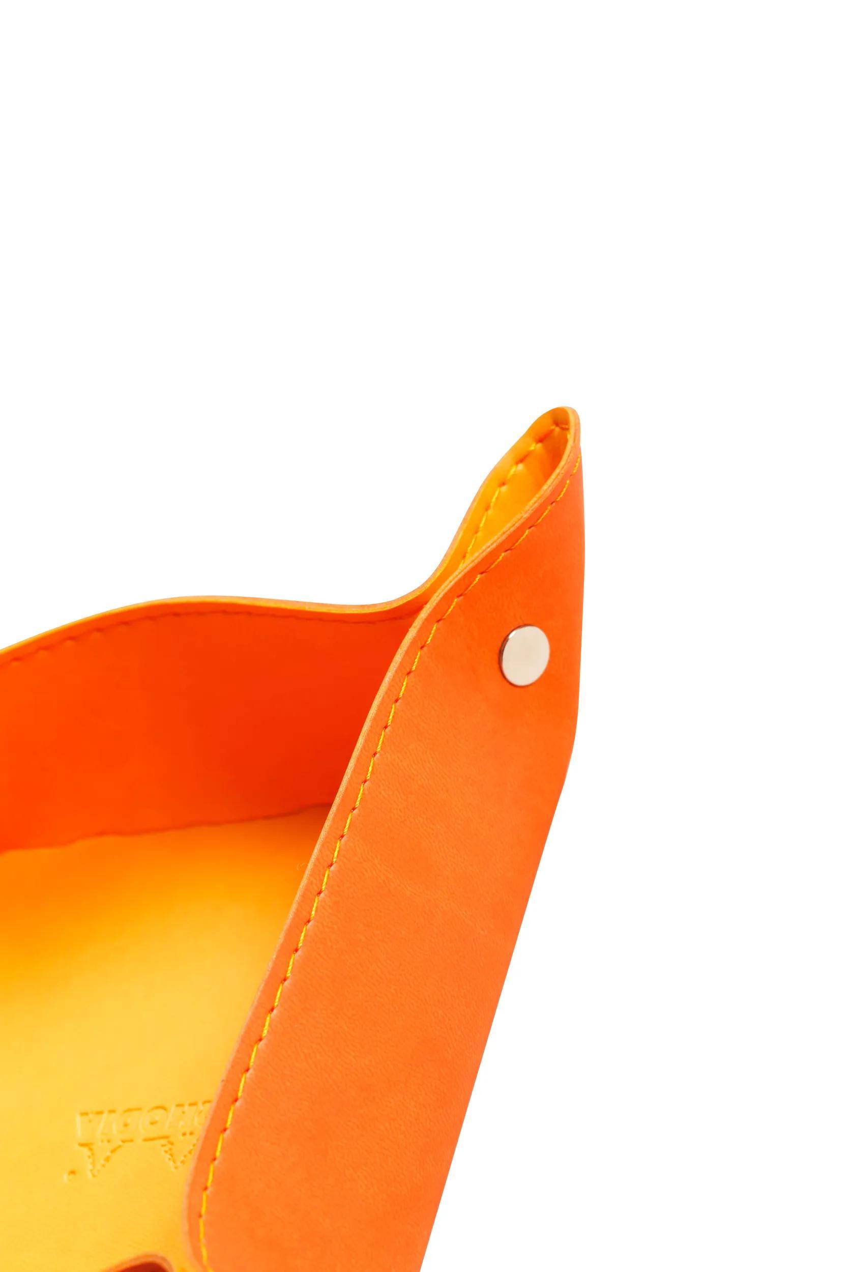 Ein orangefarbenes Ledertablett mit silbernen Druckknopfdetails in den Ecken, das das innere Futter und die Nähte zeigt.