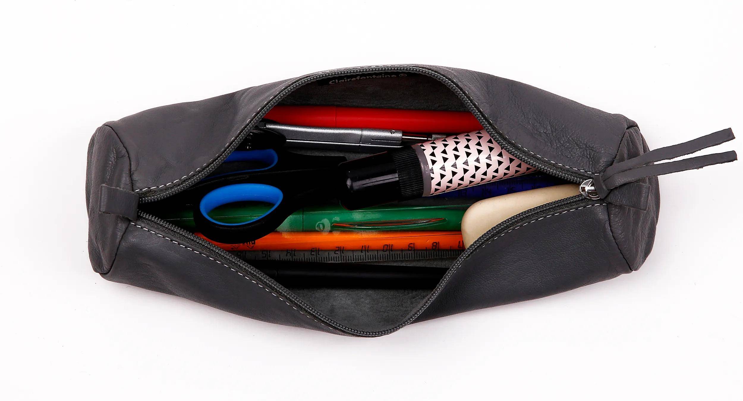 Offene schwarze Federtasche mit Reißverschluss, die Schere, Stifte, Bleistifte und kleine Schreibwaren darin auf weißem Hintergrund zeigt.