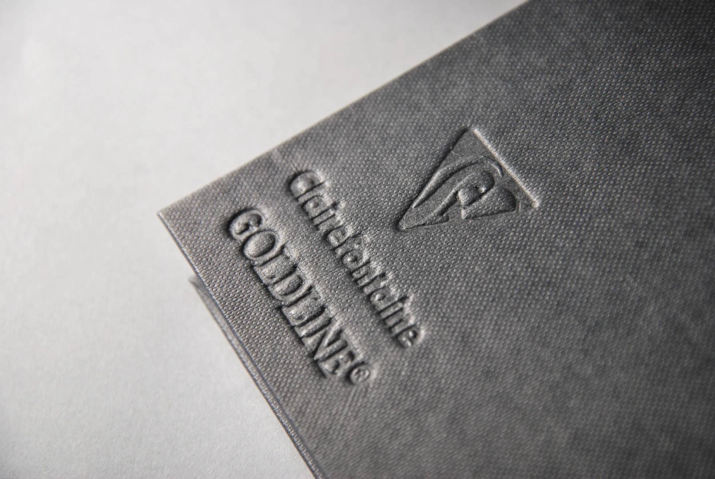 Goldline' Logo in geprägter Schrift auf einem strukturierten dunkelgrauen Hintergrund in der Ecke eines Buches oder Notizbuchs.