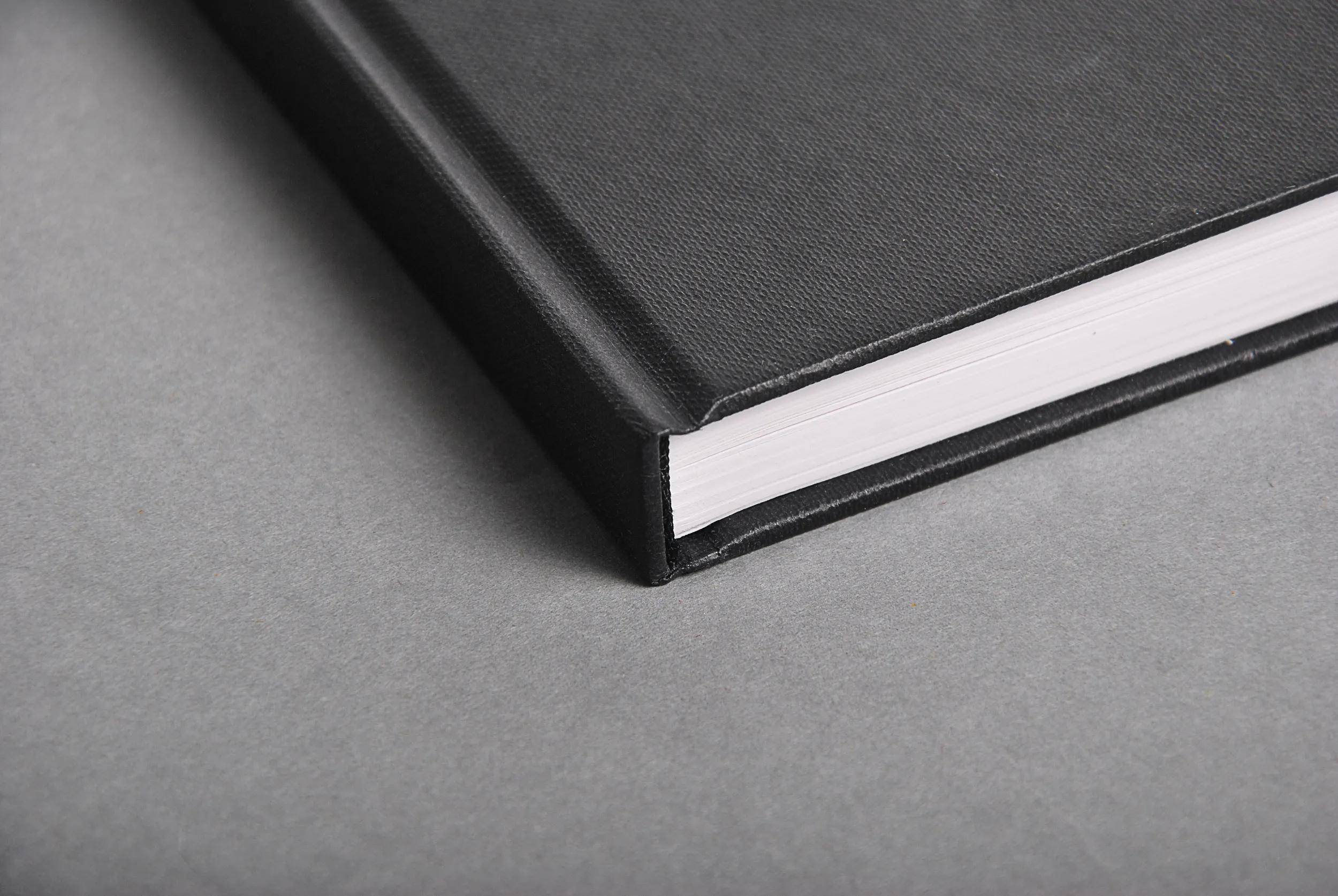 Ein geschlossenes, gebundenes Buch mit schwarzem Einband liegt auf einer grauen Oberfläche, so dass seine Kante schräg zu sehen ist.