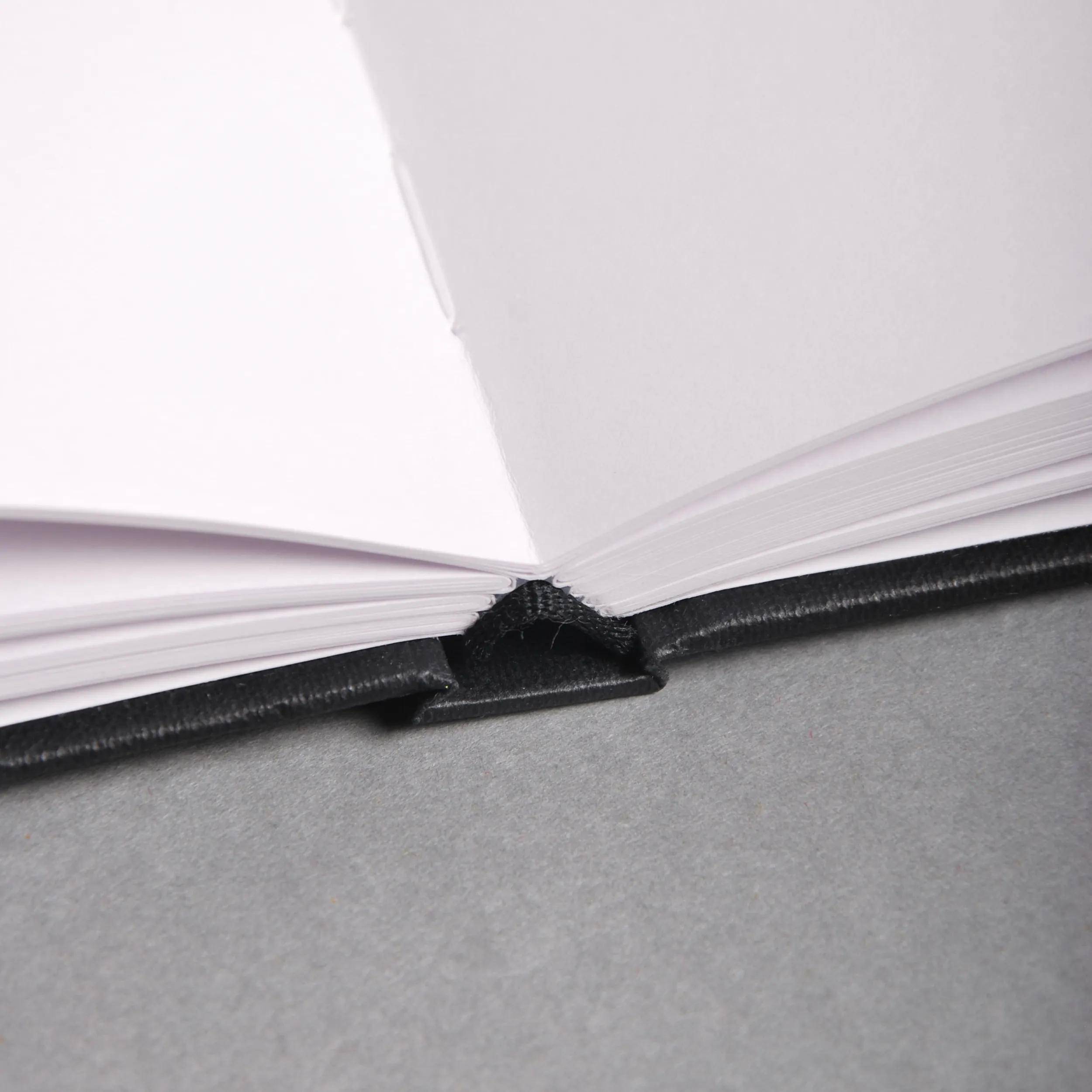 Ein aufgeschlagenes Hardcover-Buch liegt flach auf einer grauen Oberfläche, wobei der Fokus auf dem Buchrücken und den leicht aufgefächerten Seiten liegt.