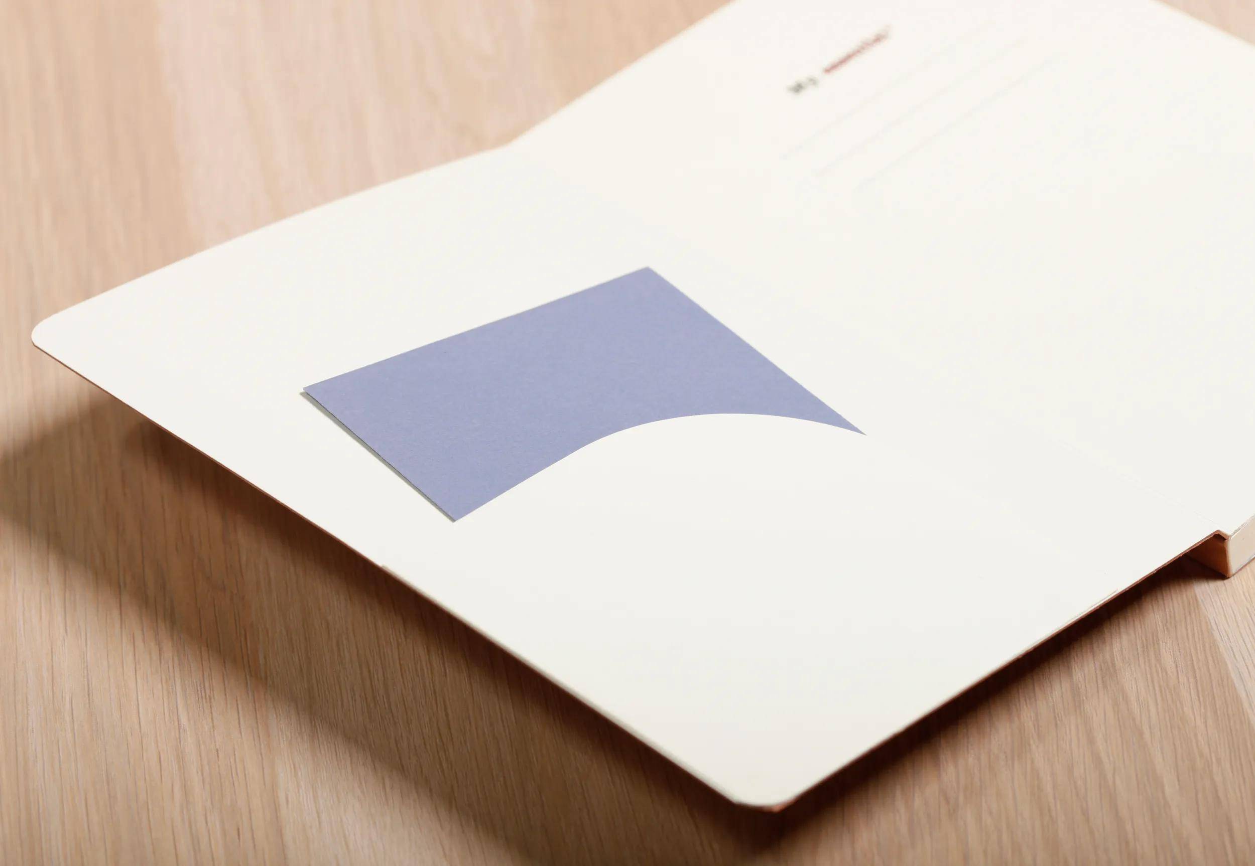 Weißer Ordner oder Umschlag auf einer Holzoberfläche, mit einem zentrierten blauen geometrischen Logo auf dem Deckblatt.