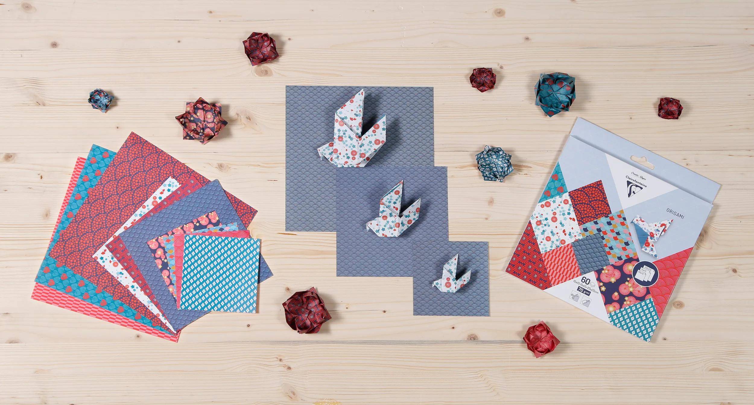 Origami-Papierhandwerksmaterialien auf einem Holztisch ausgelegt, mit gemusterten gefalteten Papierkranichen und farbigen Papieren oder Anleitunsblättern.