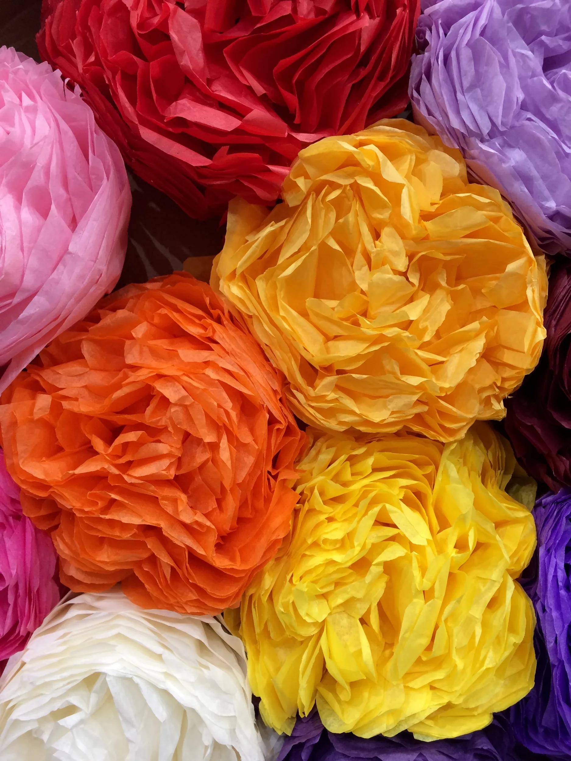 Nahaufnahme von bunten Seidenpapierblumen in Rot, Rosa, Orange, Gelb, Lila und Weiß, die dicht beieinander angeordnet sind.