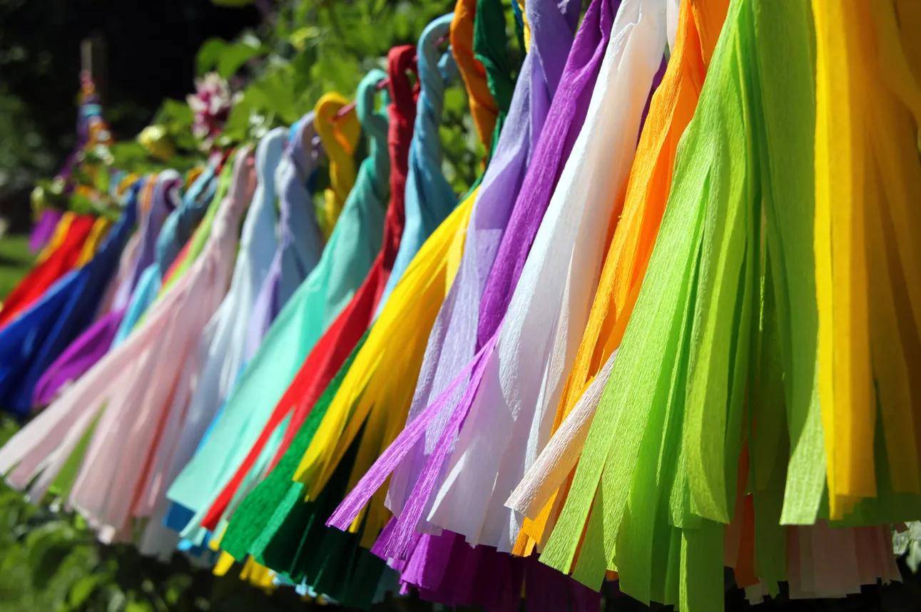 Bunte Stoffbänder oder Gebetsfahnen hängen in Reihen im Freien und flattern im Wind vor einem unscharfen grünen Hintergrund.