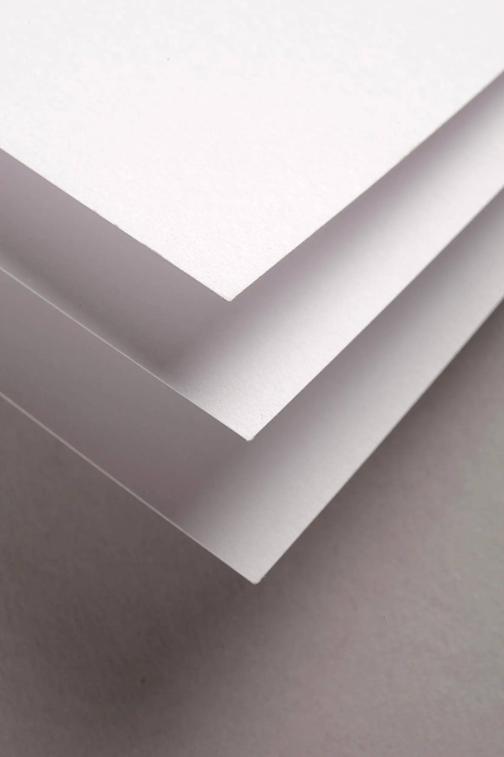 Drei gestapelte weiße Blätter Papier mit gefalteten Ecken auf grauem Hintergrund, von oben betrachtet.
