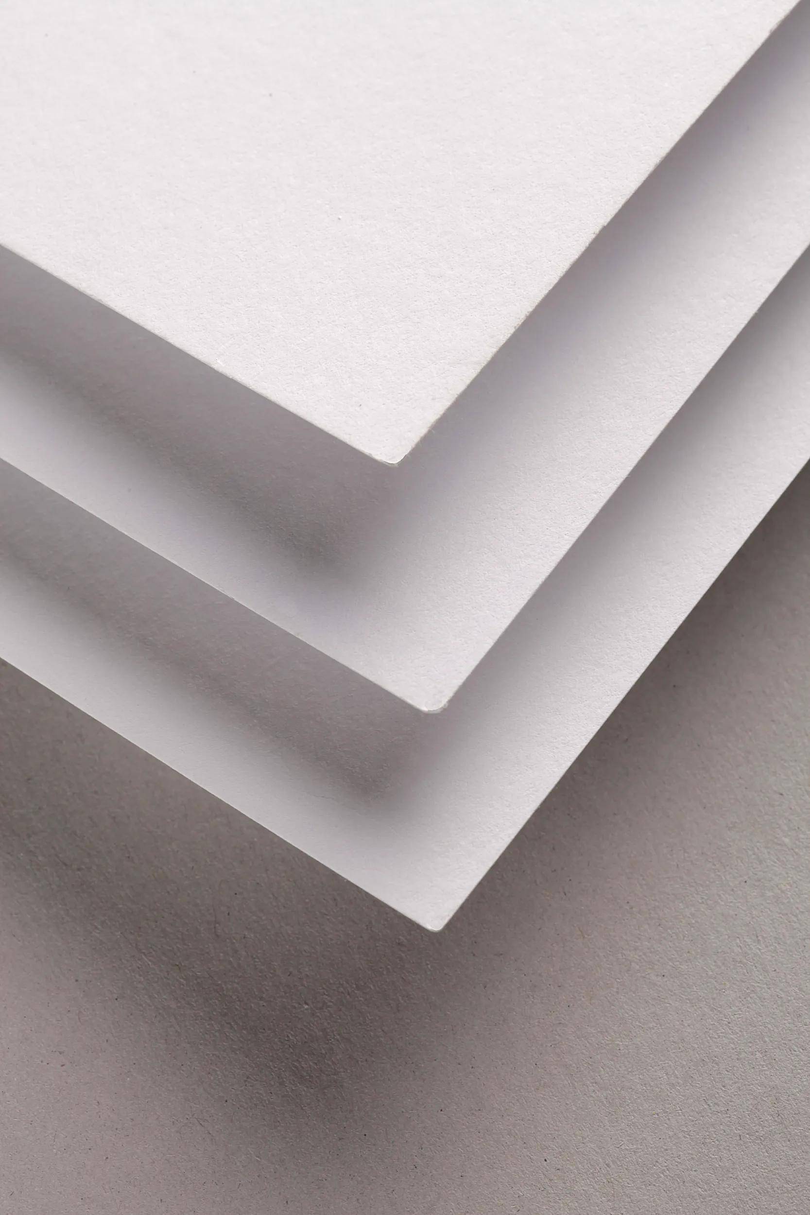 Nahaufnahme von gestapelten weißen Papiertüchern mit geschichteten Ecken, die eine diagonale V-Form vor einem grauen Hintergrund bilden.