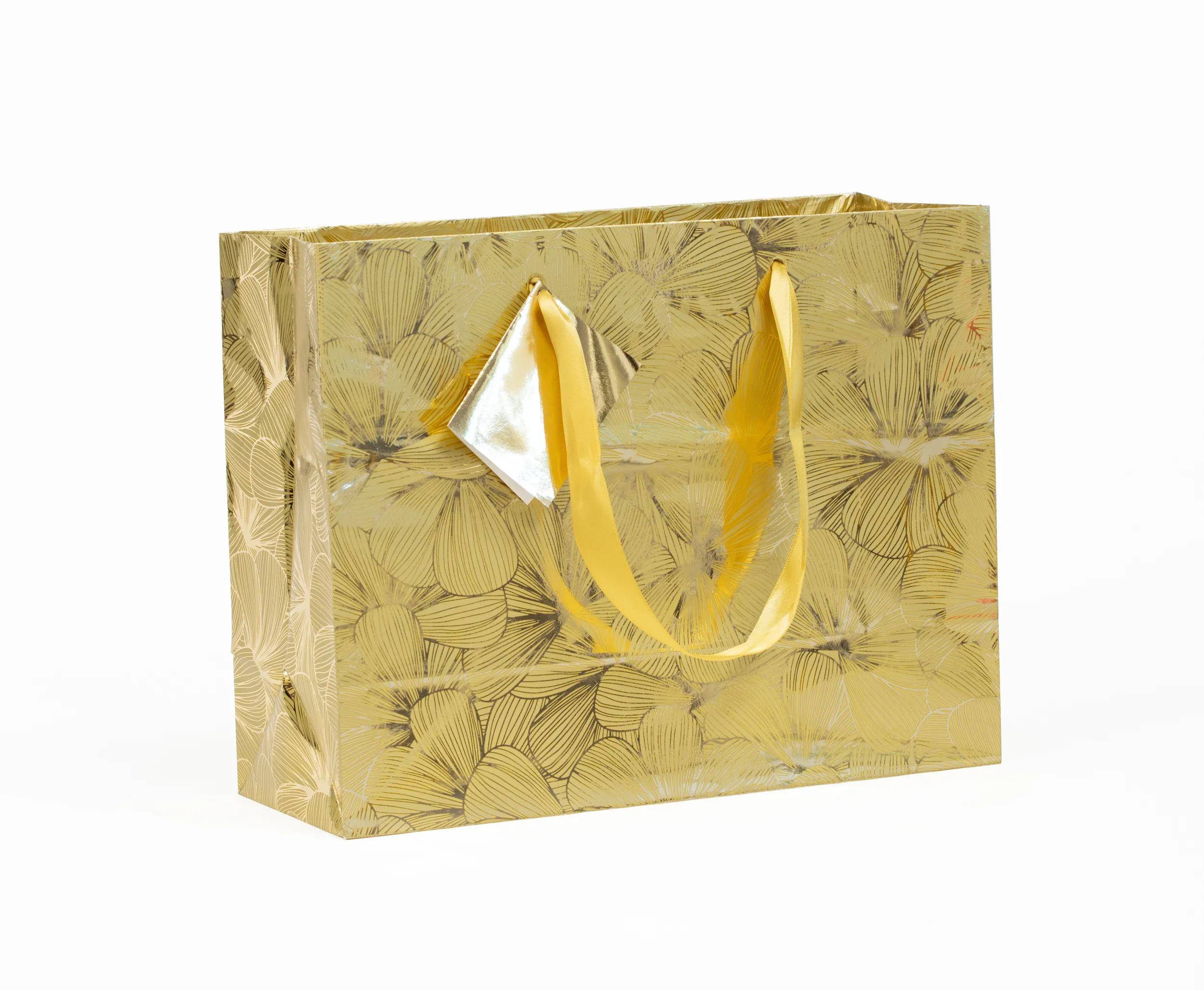 Goldfarbene Geschenktasche mit Blumenmuster und gelben Griffbändern auf weißem Hintergrund.