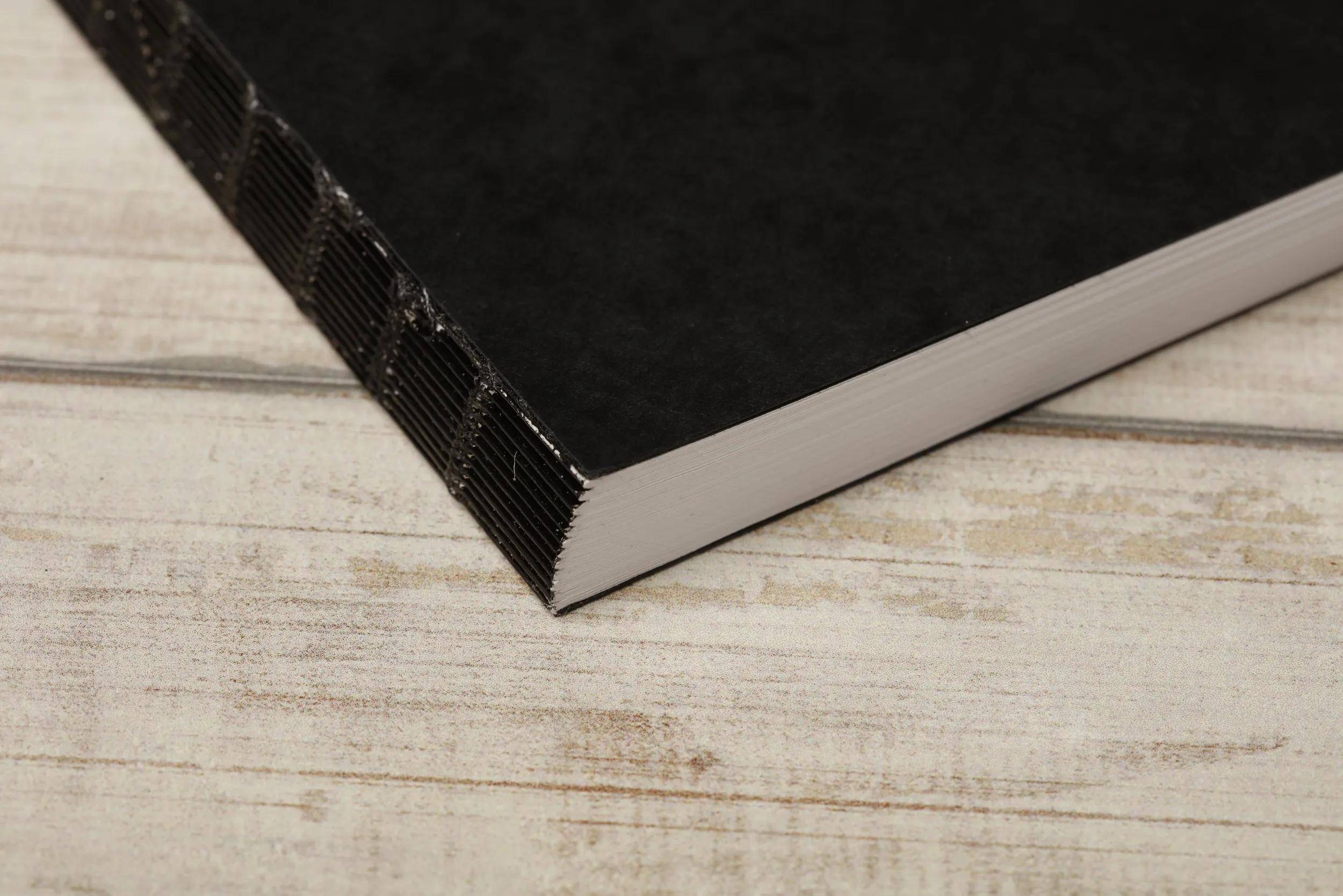 Nahaufnahme eines schwarzen Hardcover-Buches, das auf einer hellen Holzoberfläche ruht, wobei der Buchrücken und die Buchkanten sichtbar sind.