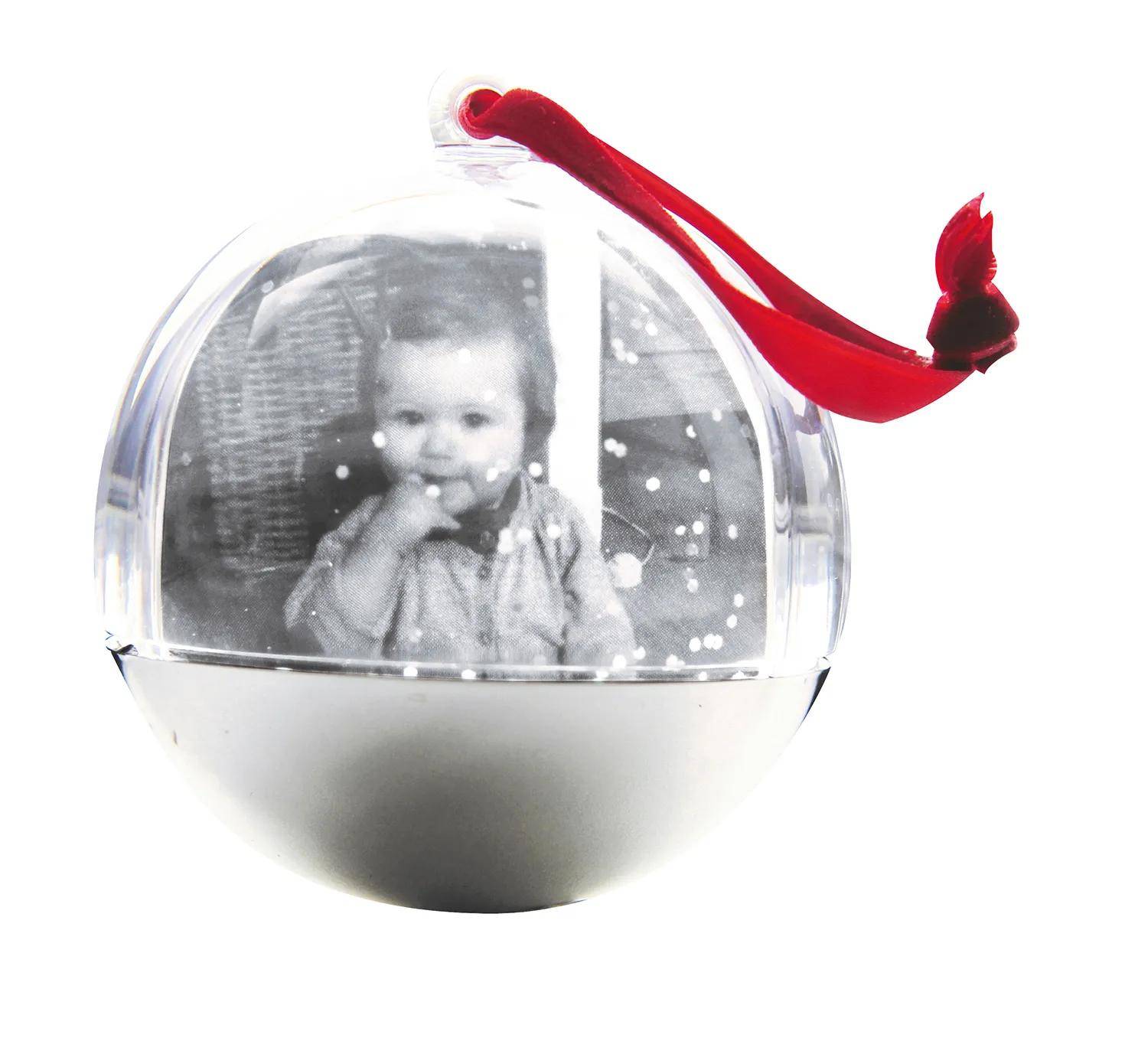 Klare Glaskugel für Weihnachten mit einem schwarz-weißen Babyfoto im Inneren und einem roten Aufhängeband auf weißem Hintergrund.