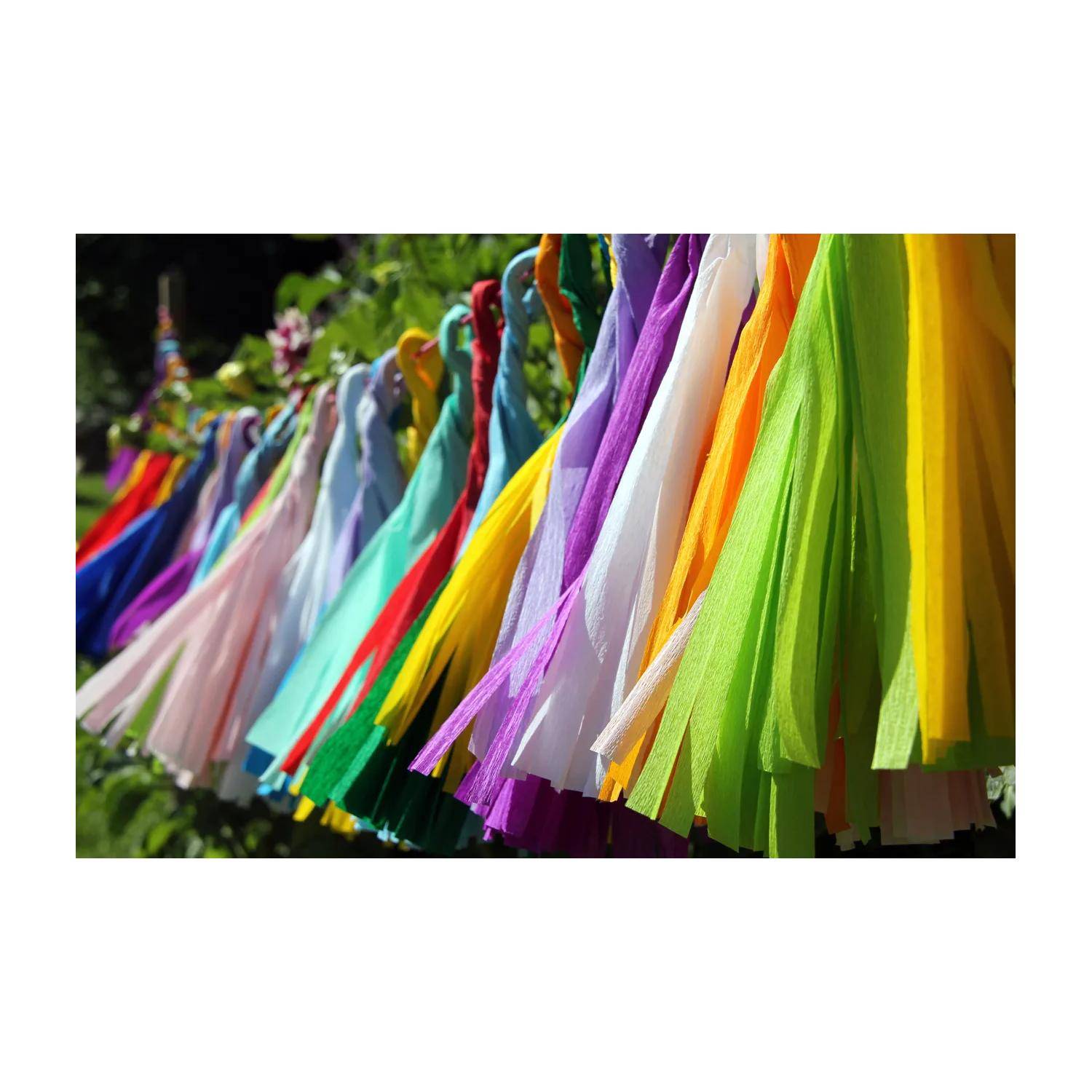 Bunte Quasten oder Bänder, die in einer Reihe im Freien hängen, mit leuchtend gelben, grünen, violetten, weißen und rosa Streifen im Vordergrund.