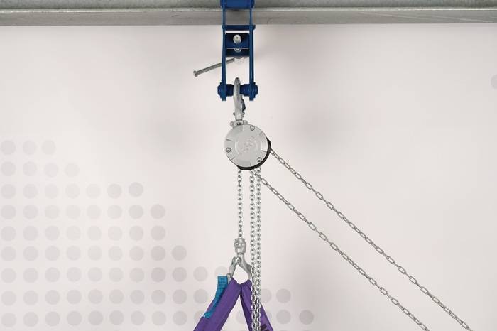 Blauer Kettenzug mit Ketten, die ein violettes Hebetuch gegen eine weiße Wand und Decke hebt.