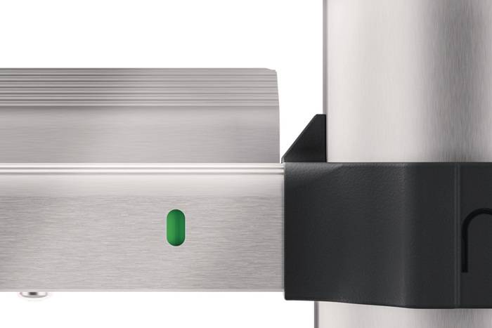 Nahaufnahme einer gebürsteten Metallverriegelungsklinke oder Klammer mit einem kleinen grünen Indikator, befestigt an einem vertikalen silbernen Pfosten.