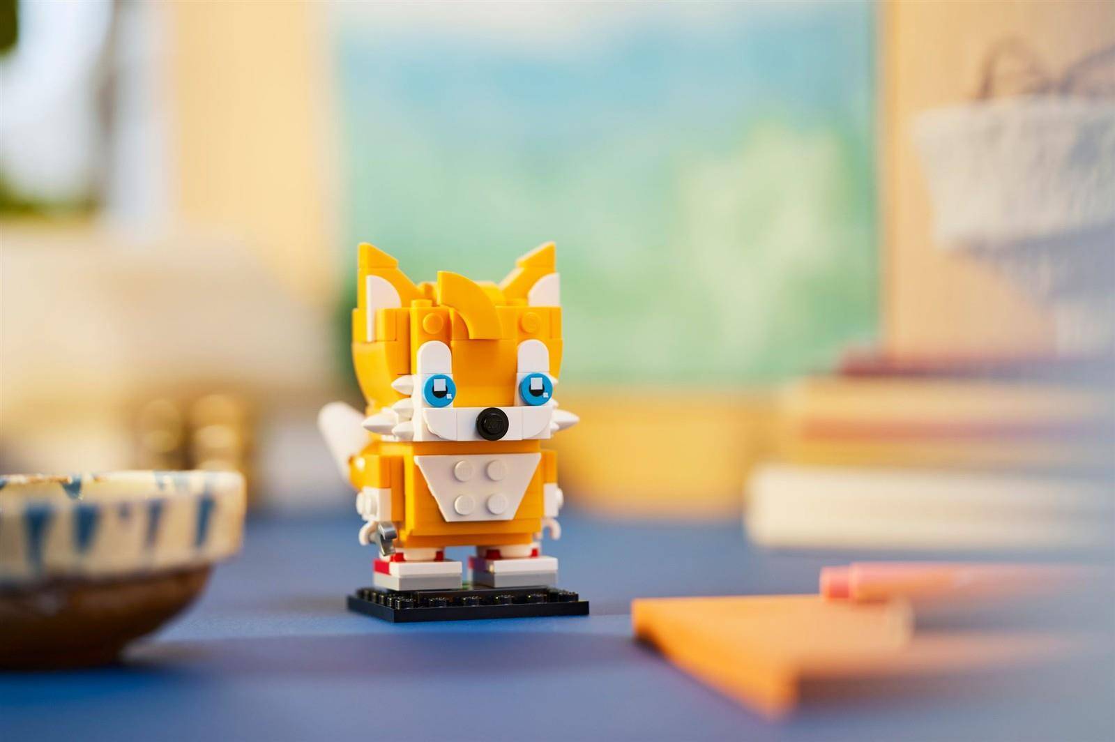 Kleine orange-weiße Fuchs-LEGO-Figur, die auf einer Tischplatte steht, mit unscharfem Raum im Hintergrund.