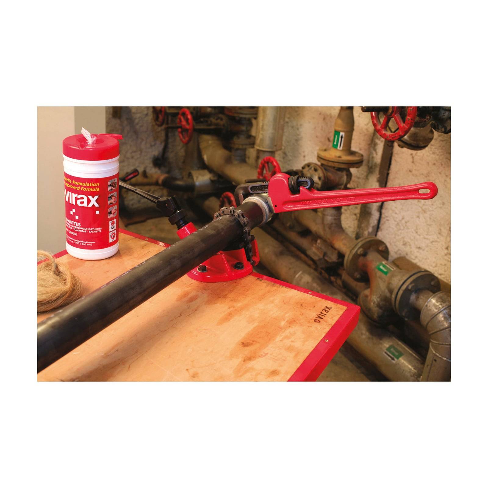 Ein Rohrzange auf einer Werkbank wird zum Festziehen von Klempnerröhren verwendet. Im Hintergrund sind Rohre und rote Ventilgriffe zu sehen.