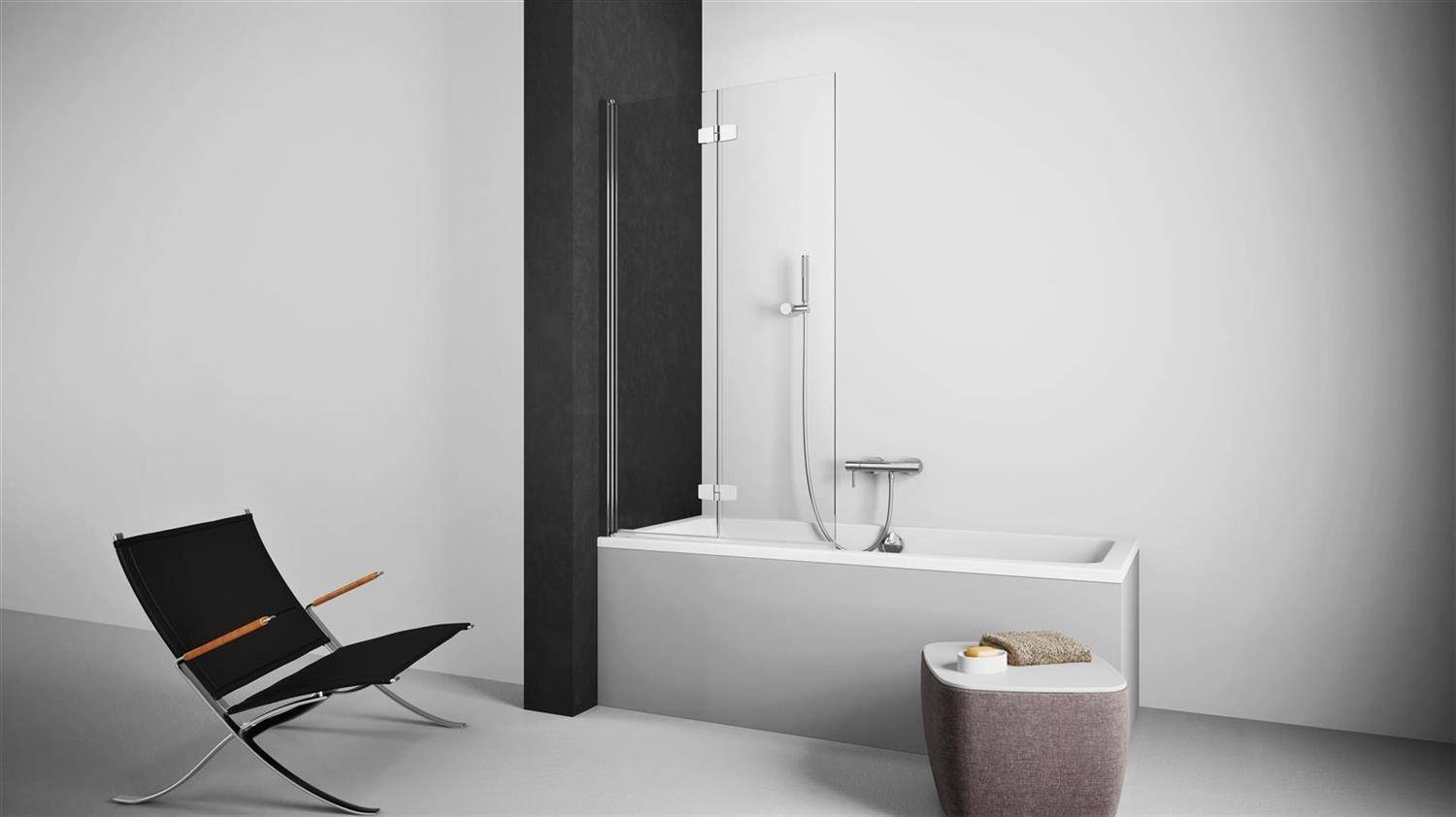 Minimales modernes Badezimmer mit freistehender weißer Badewanne und Glasschiebetür für die Dusche, schwarzem Trennpanel, Loungesessel und geflochtenem Hocker mit Handtuch.
