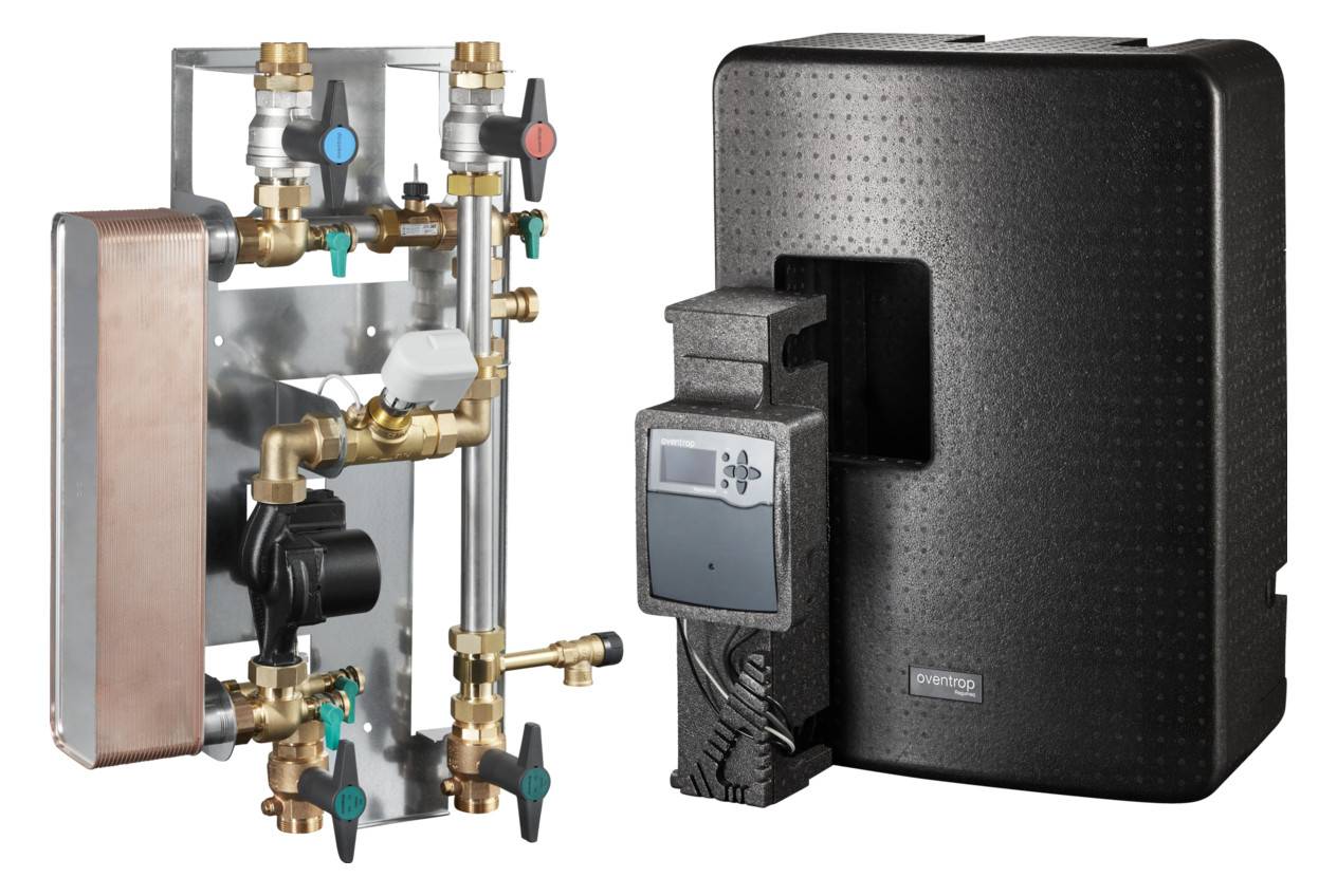 Heizungsregelanlage mit schwarzer isolierter Abdeckung, Anzeigemodule und freiliegende Metallventile, Rohre und Pumpenanlage daneben.