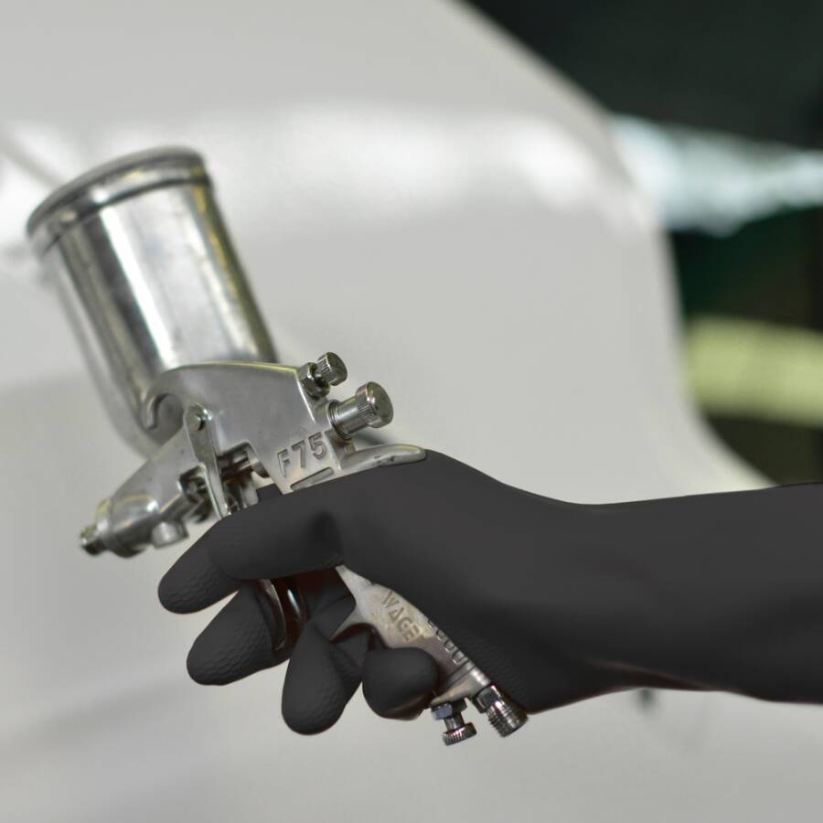 Behandschuhte Hand hält eine Metallspritzpistole oder Airbrush mit kleinem Farbbehälter, bereit zum Anstreichen oder Beschichten.