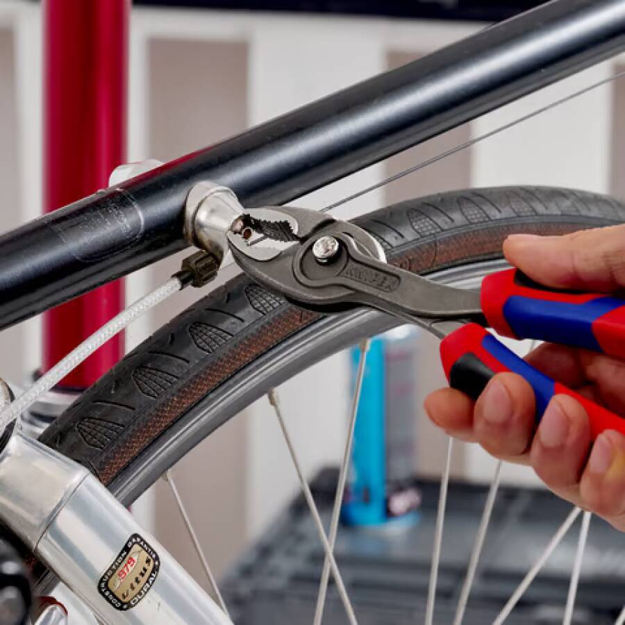 Nahaufnahme einer Zange, die ein Fahrradbremskabel in der Nähe des Rades und Rahmens während einer Reparatur oder Einstellung hält.