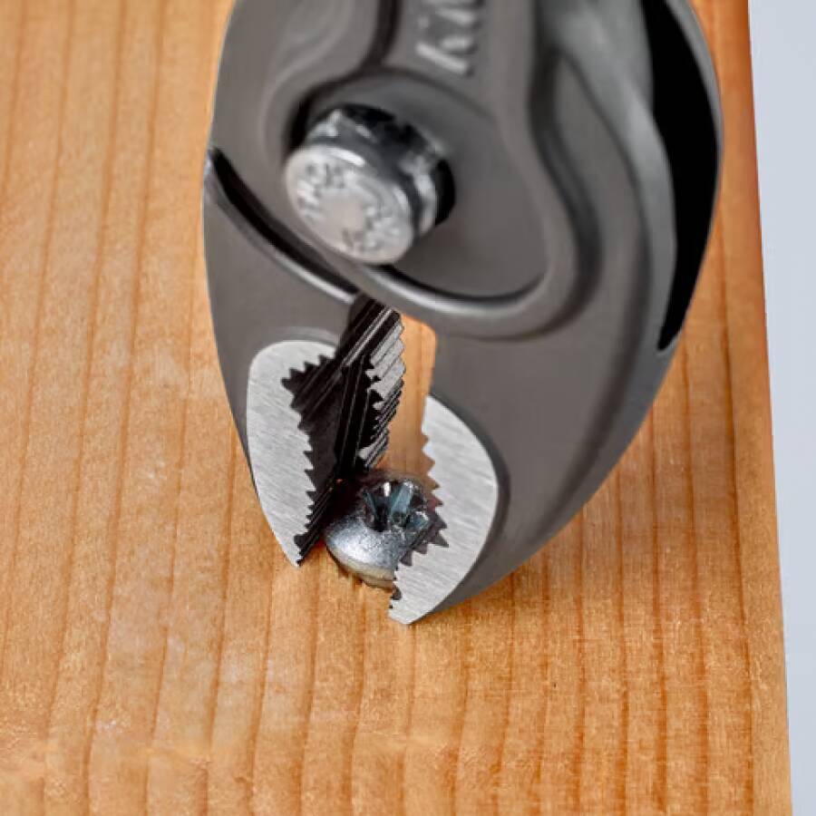 Nahaufnahme einer Zange, die eine in ein Holzbrett eingebettete Schraube erfasst und lockert.