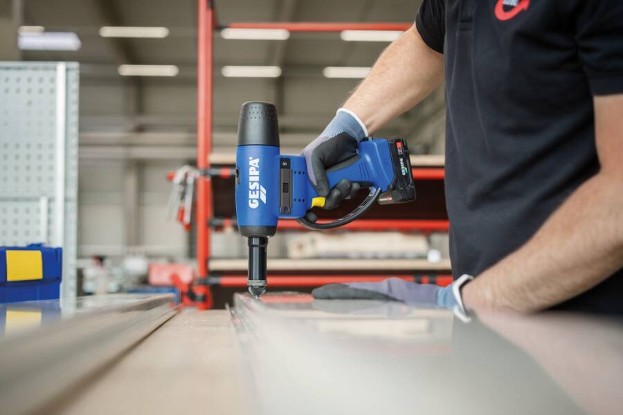 Arbeiter mit einem blauen tragbaren Gesipa-Nietewerkzeug zum Befestigen von Metall auf einer Werkbank in einer Werkstatt.
