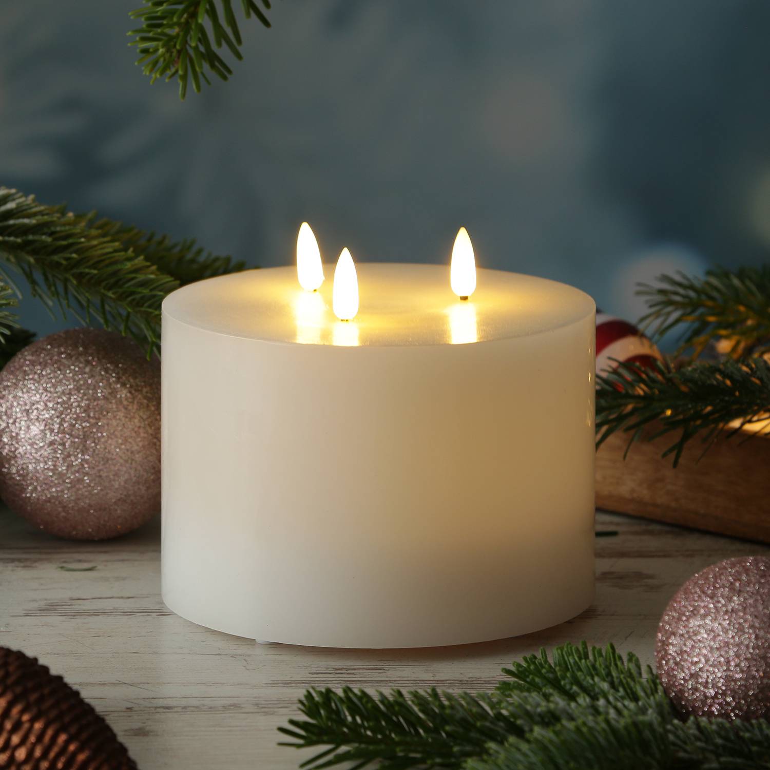 Eine beleuchtete weiße Kerze mit drei Flammen, platziert zwischen Tannenzweigen, glitzernden Weihnachtsschmuck und Zuckerstangen, die eine festliche Weihnachtsatmosphäre erzeugt.