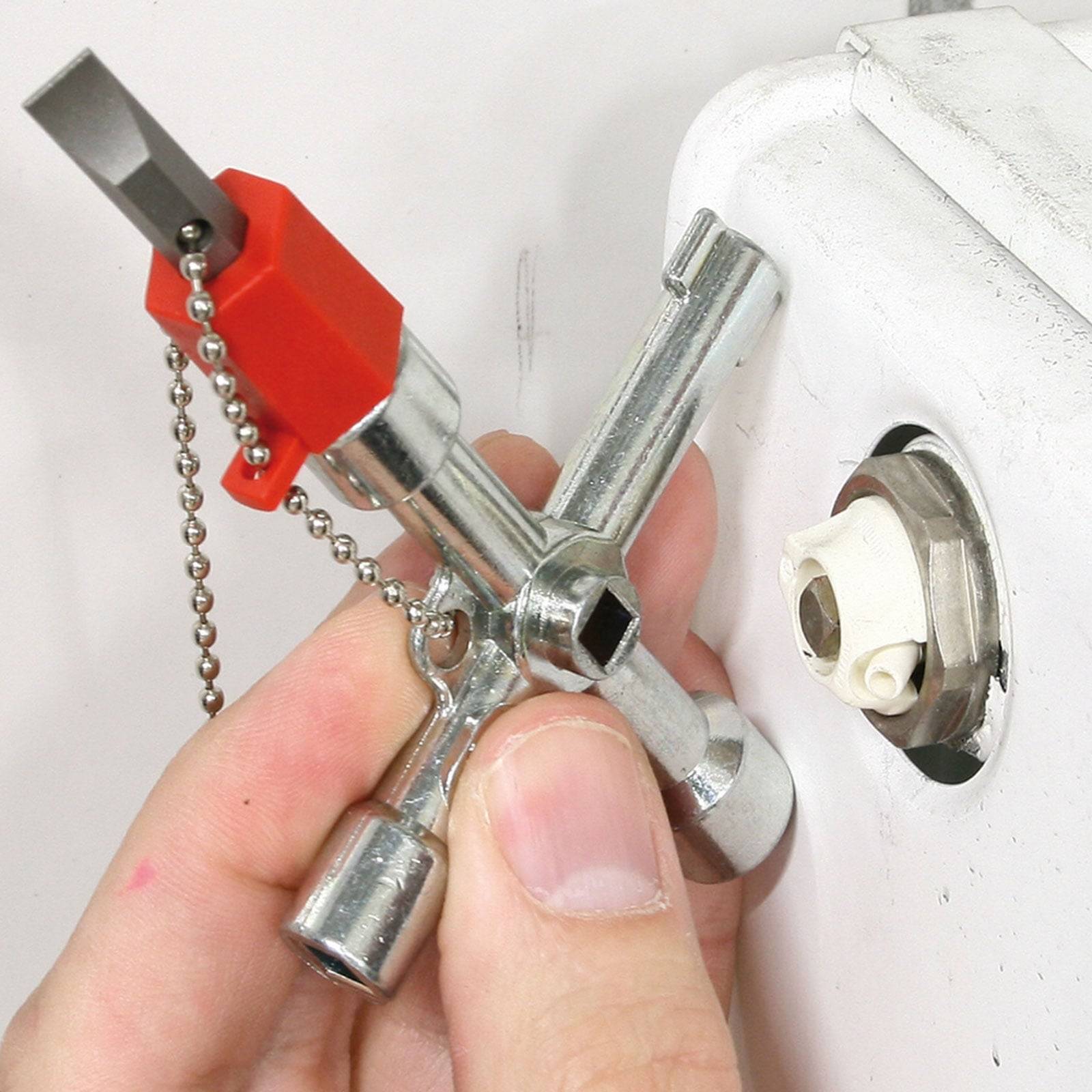 Eine Hand hält einen kleinen, metallenen Multifunktions-Schlüssel für Versorgungsschränke, mit einer roten Befestigung und Kette. Das Werkzeug wird in eine gesicherte Abdeckung eingeführt.