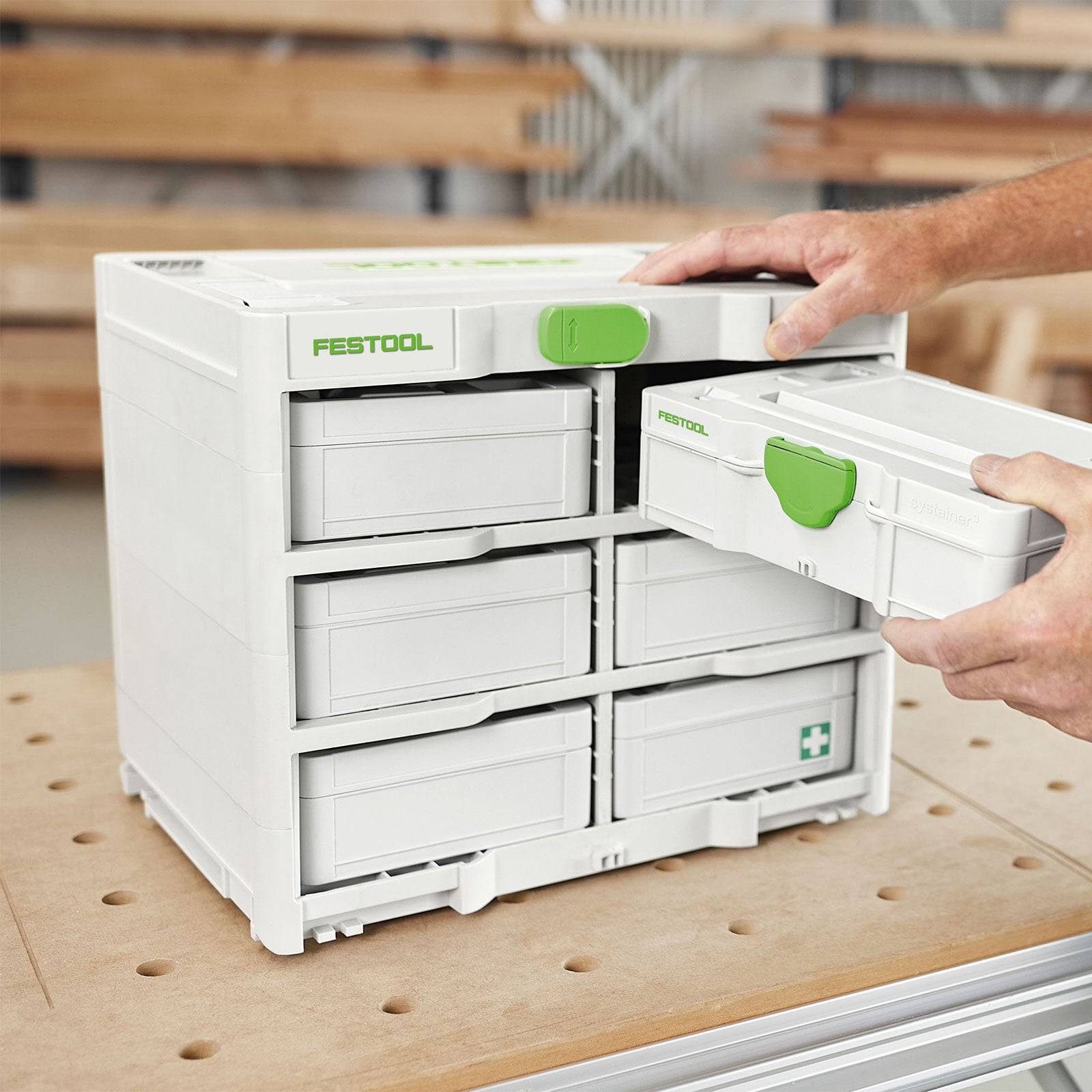 Eine Person, die eine weiße Festool-Aufbewahrungseinheit mit grünen Griffen auf einer Werkbank organisiert, wobei die zahlreichen Schubladen und Fächer hervorgehoben werden.