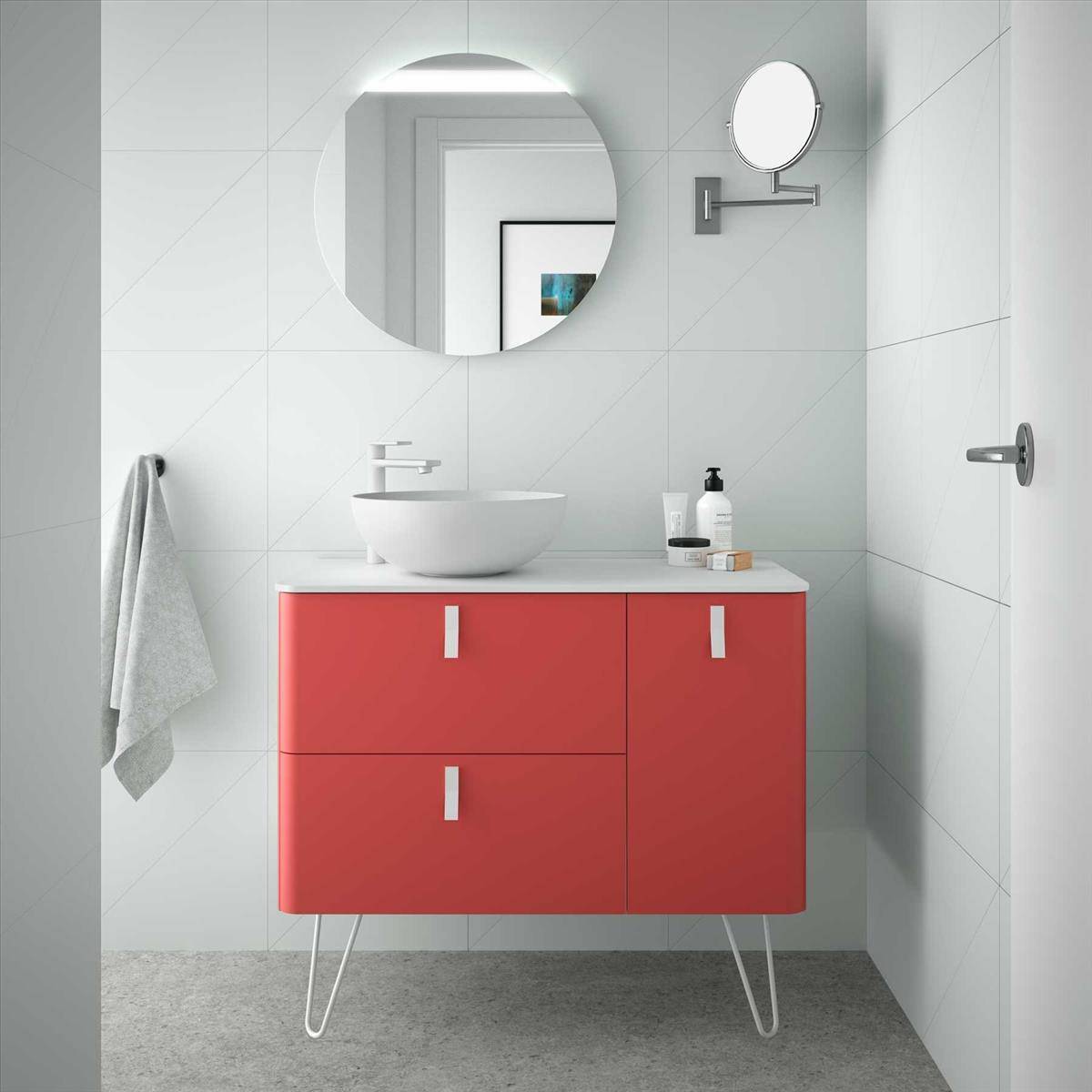 Modernes Badezimmer mit an der Wand montiertem roten Waschtisch, weißem Aufsatzwaschbecken, rundem Spiegel, Handtuch und Toilettenartikeln vor hellem Fliesengrund.