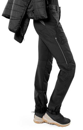 Eine Person, die eine schwarze Jacke und schwarze Hose trägt, von Hals abwärts abgebildet, vor einem schwarzen Hintergrund. Der Fokus liegt auf dem Kleidungsstil.