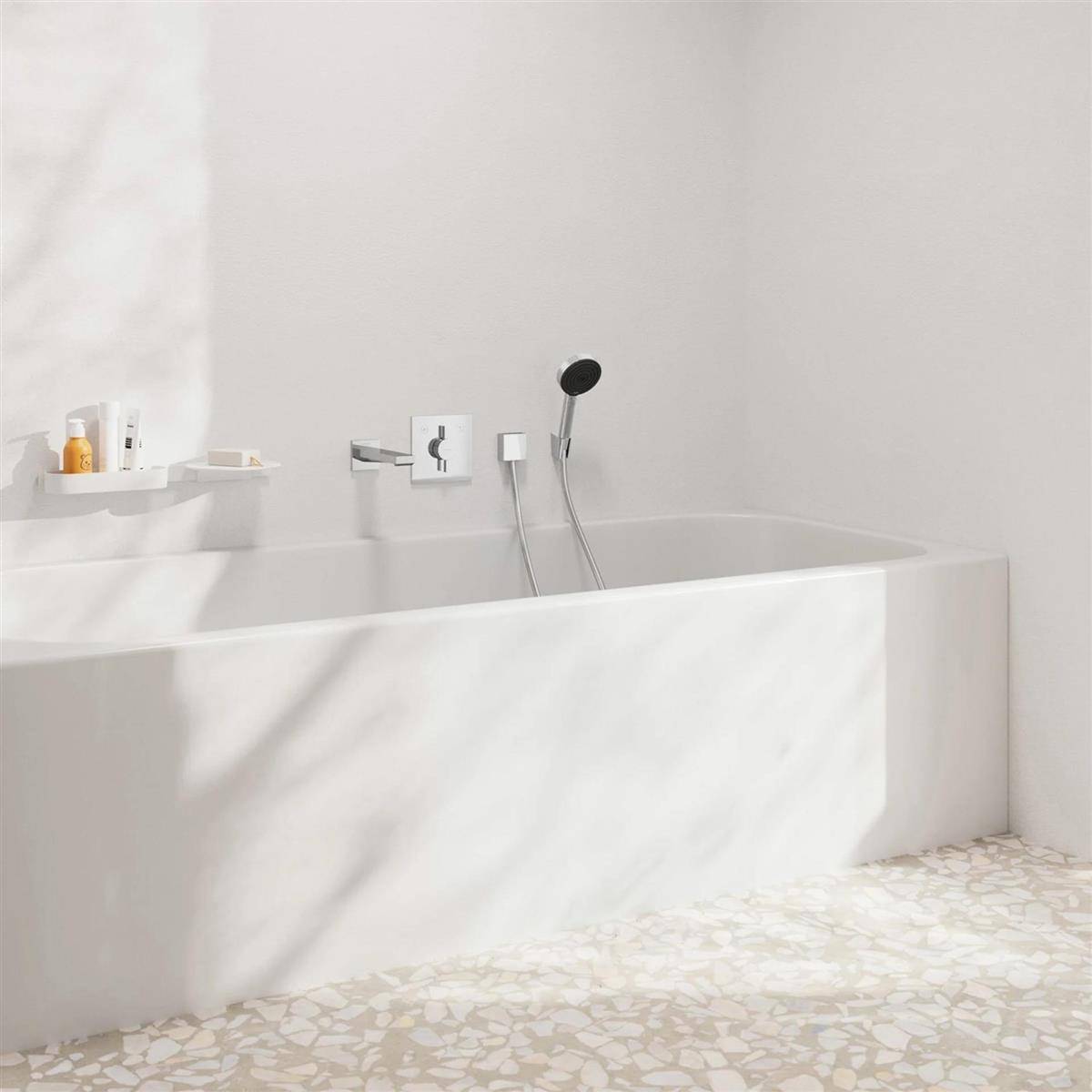 Minimales weißes Badezimmer mit einer modernen eingebauten Badewanne, an der Wand montierten Armaturen und Sonnenlicht, das Schatten über die Badewanne und den gemusterten Boden wirft.