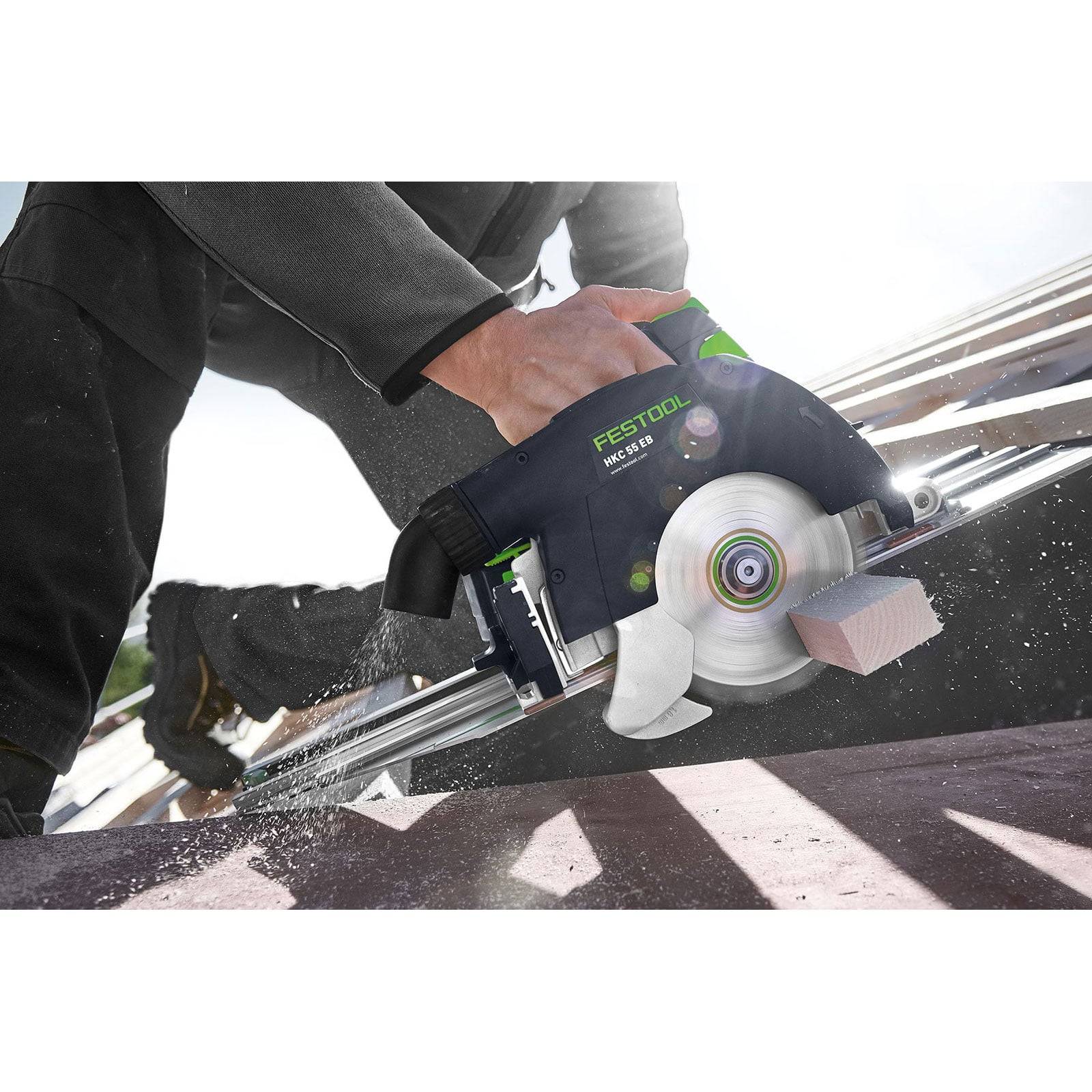 Eine Person verwendet eine Festool Kreissäge, um Holzbretter zu durchtrennen, wobei Sägespäne entstehen. Die Säge ist schwarz und grün mit einer sichtbaren Sägeblatt.