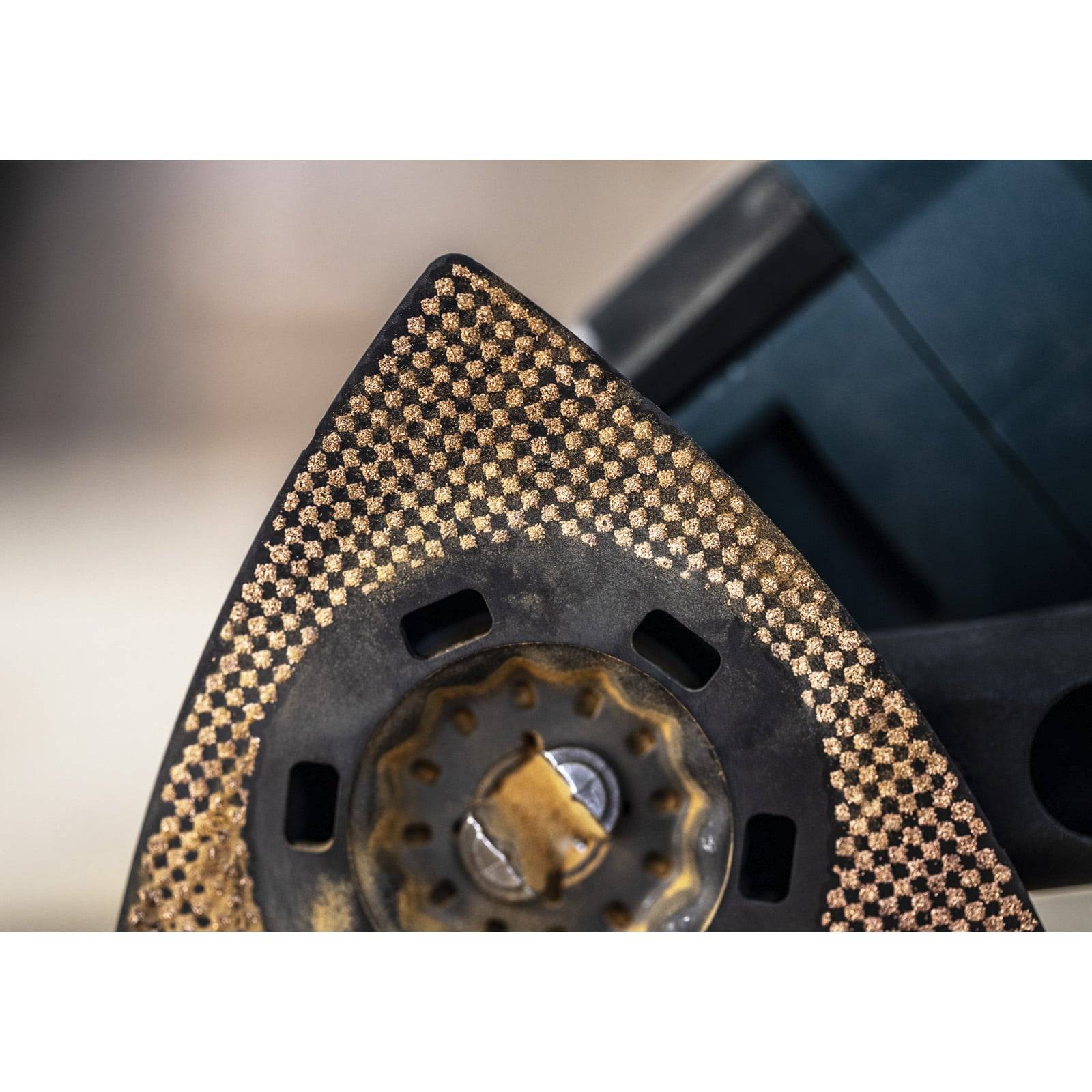 Nahaufnahme eines strukturierten Werkzeugkopfes mit einer goldfarben perforierten Oberfläche, der an einem schwarzen Gerät befestigt ist und industrielle Verwendung andeutet.