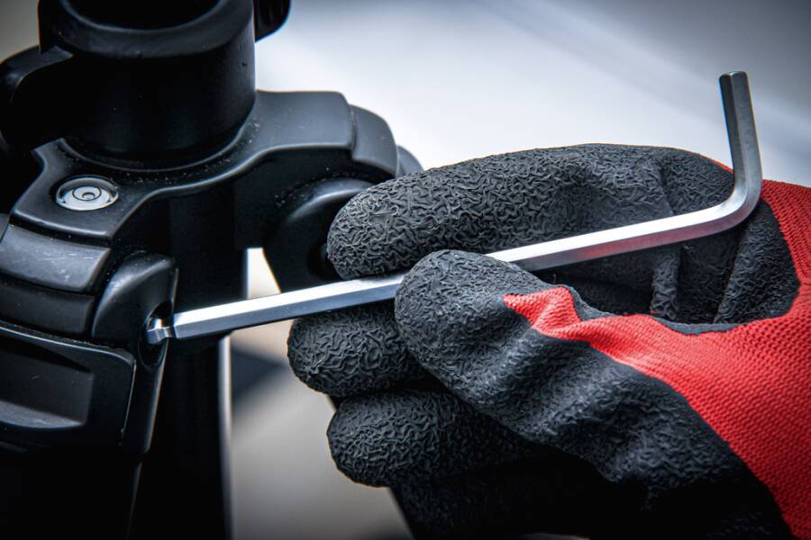 Mit Handschuh bekleidete Hand verwendet einen L-förmigen Inbusschlüssel, um eine Schraube an einem schwarzen mechanischen Gerät festzuziehen.